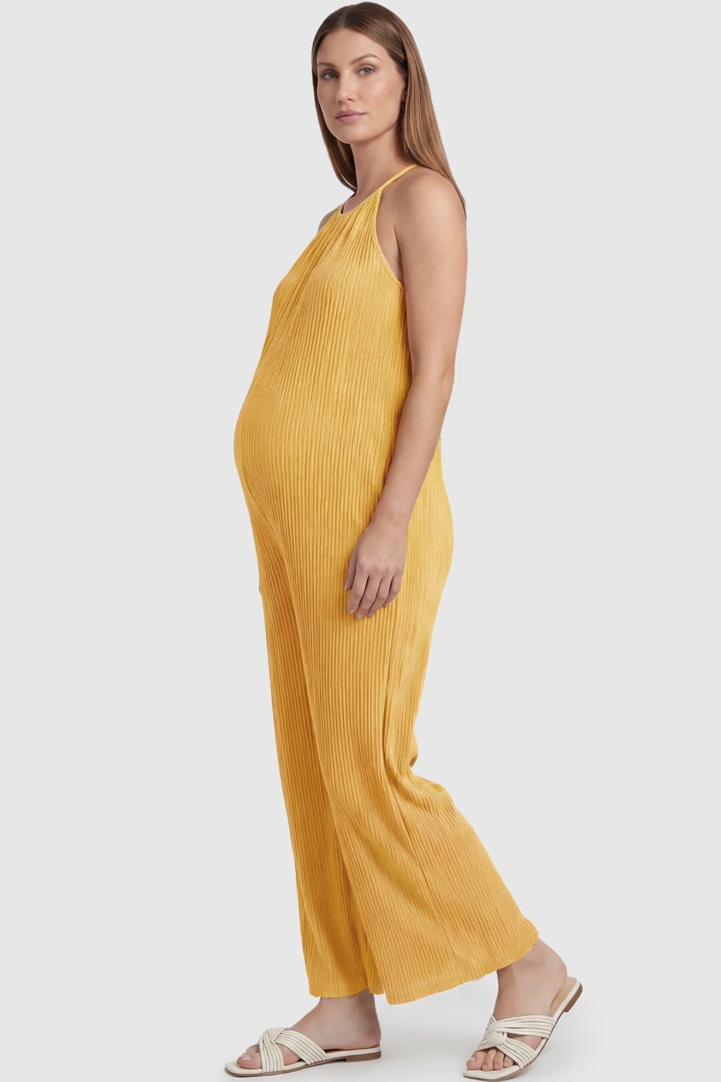 Halter Neck Wide Leg Pocketed Maternity Jumpsuit Halter Neck Wide Leg Pocketed Maternity Jumpsuit in Yellow featuring a ribbed halter neck design on a pregnant model, side view.