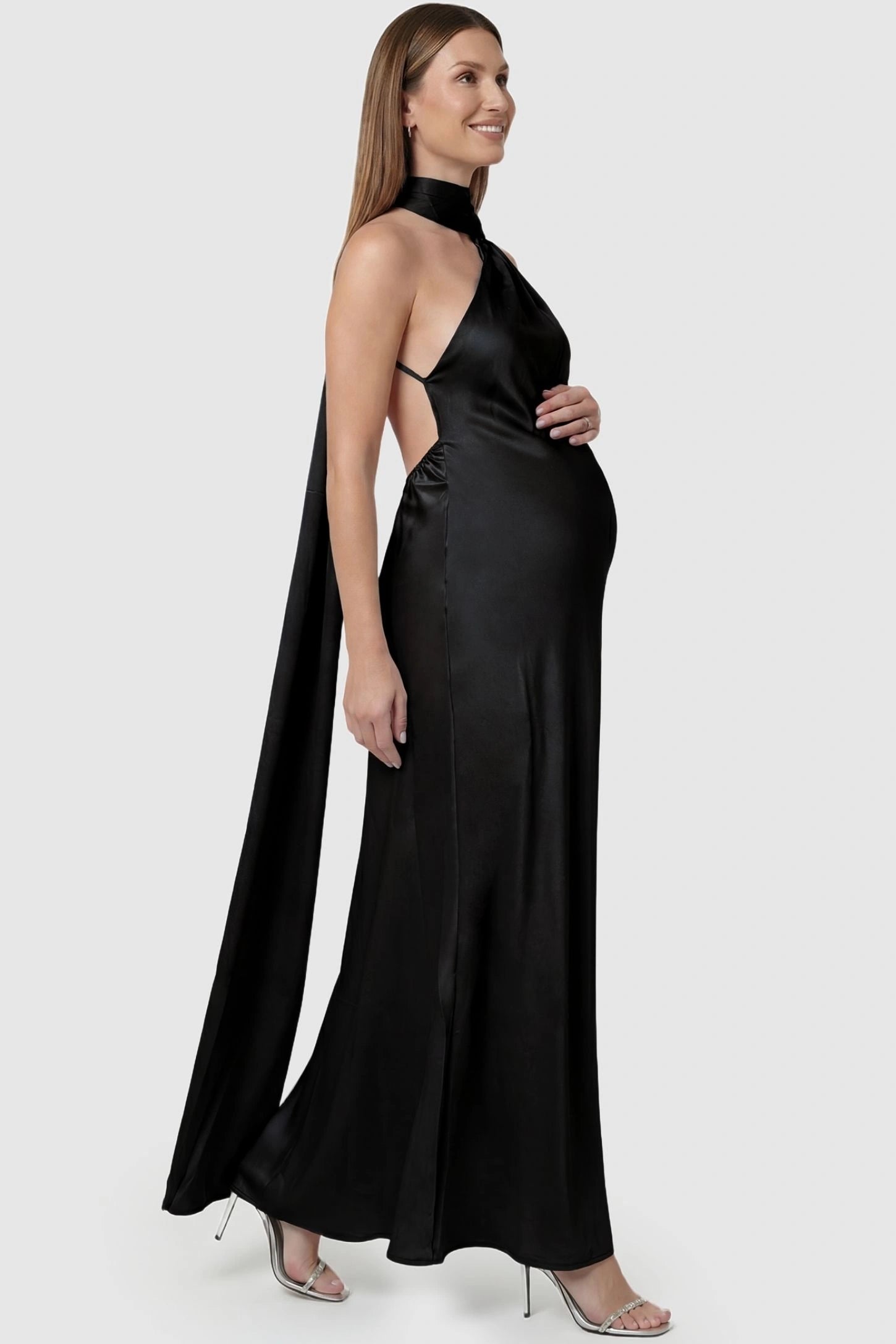 High-Shine Halter Sleeveless Maternity Maxi Dress High-Shine Halter Sleeveless Maternity Maxi Dress in Black featuring a trailing back sash on a pregnant model, side view.