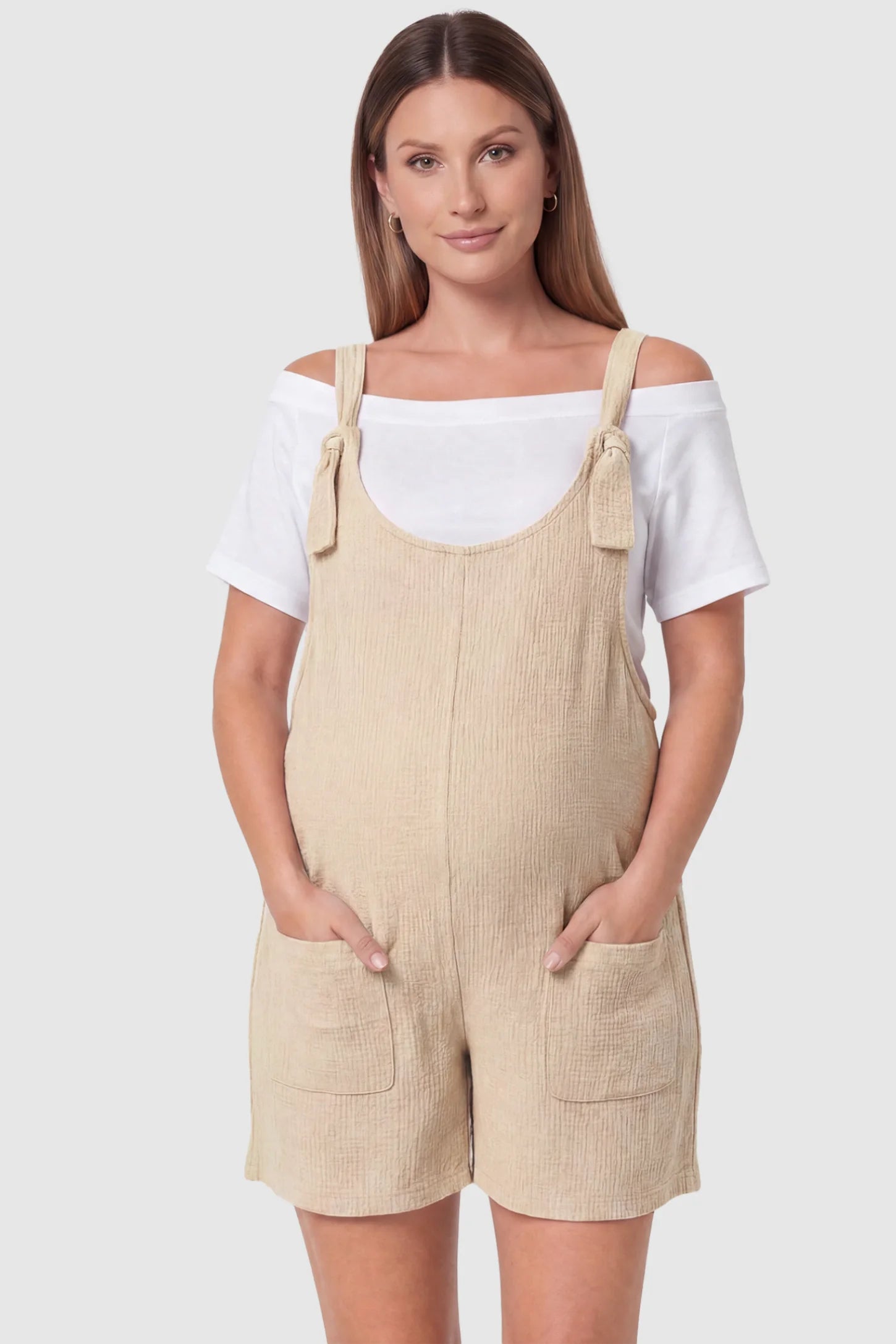 Knot Strap Front Pocket Maternity Romper Knot Strap Front Pocket Maternity Romper in Beige featuring deep front pockets and a scoop neck on a pregnant model, front view.