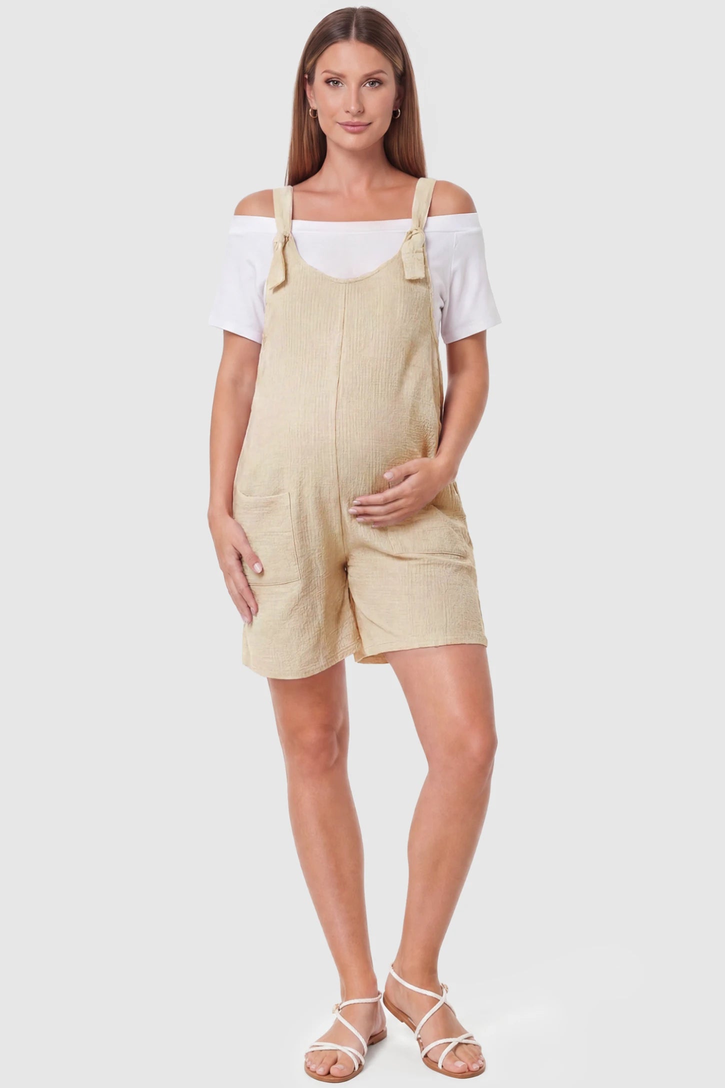 Knot Strap Front Pocket Maternity Romper Knot Strap Front Pocket Maternity Romper in Beige featuring deep front pockets and a scoop neck on a pregnant model, full body view.