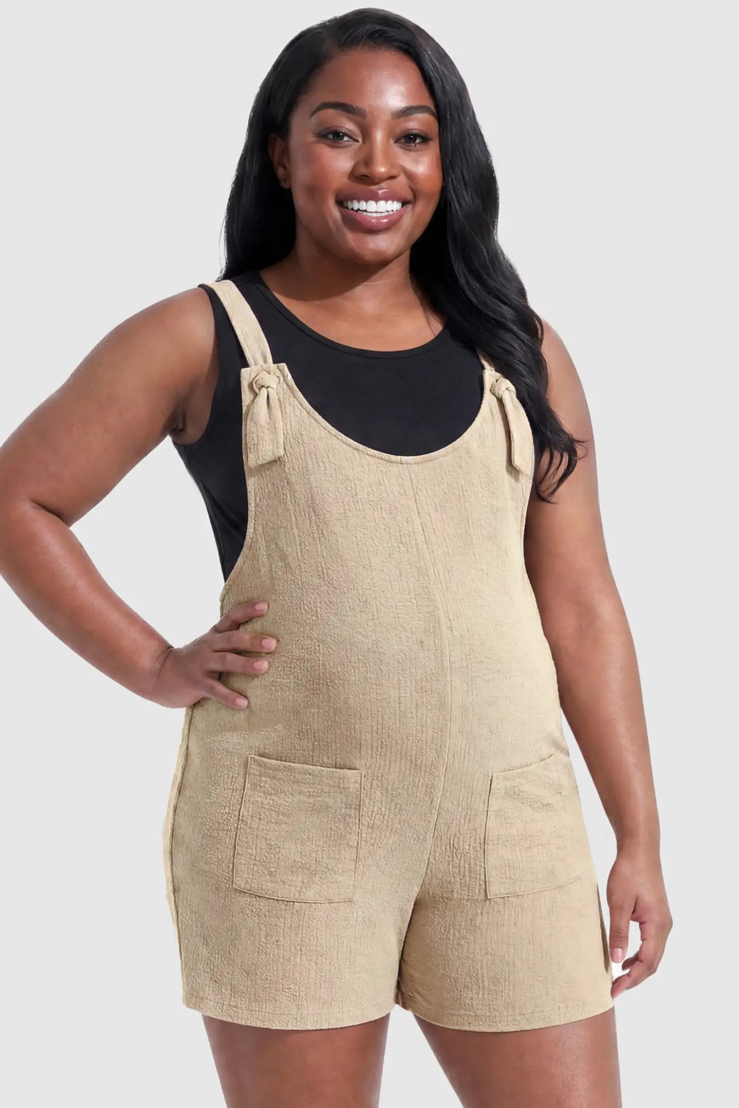 Knot Strap Front Pocket Maternity Romper Knot Strap Front Pocket Maternity Romper in Beige featuring deep front pockets and a scoop neck on a plus size pregnant model, front view.