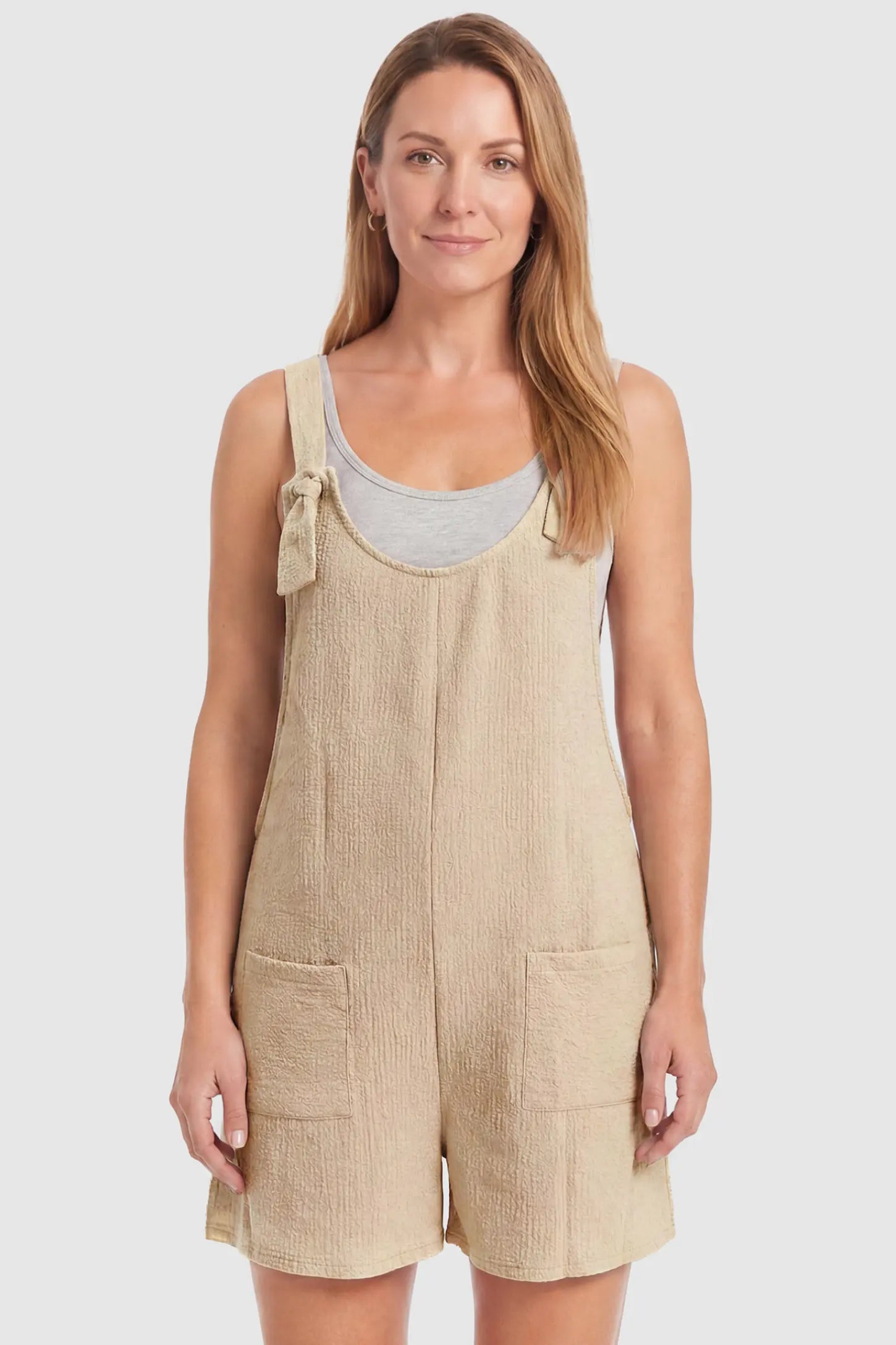 Knot Strap Front Pocket Maternity Romper Knot Strap Front Pocket Maternity Romper in Beige featuring deep front pockets and a scoop neck on a postpartum model, front view.