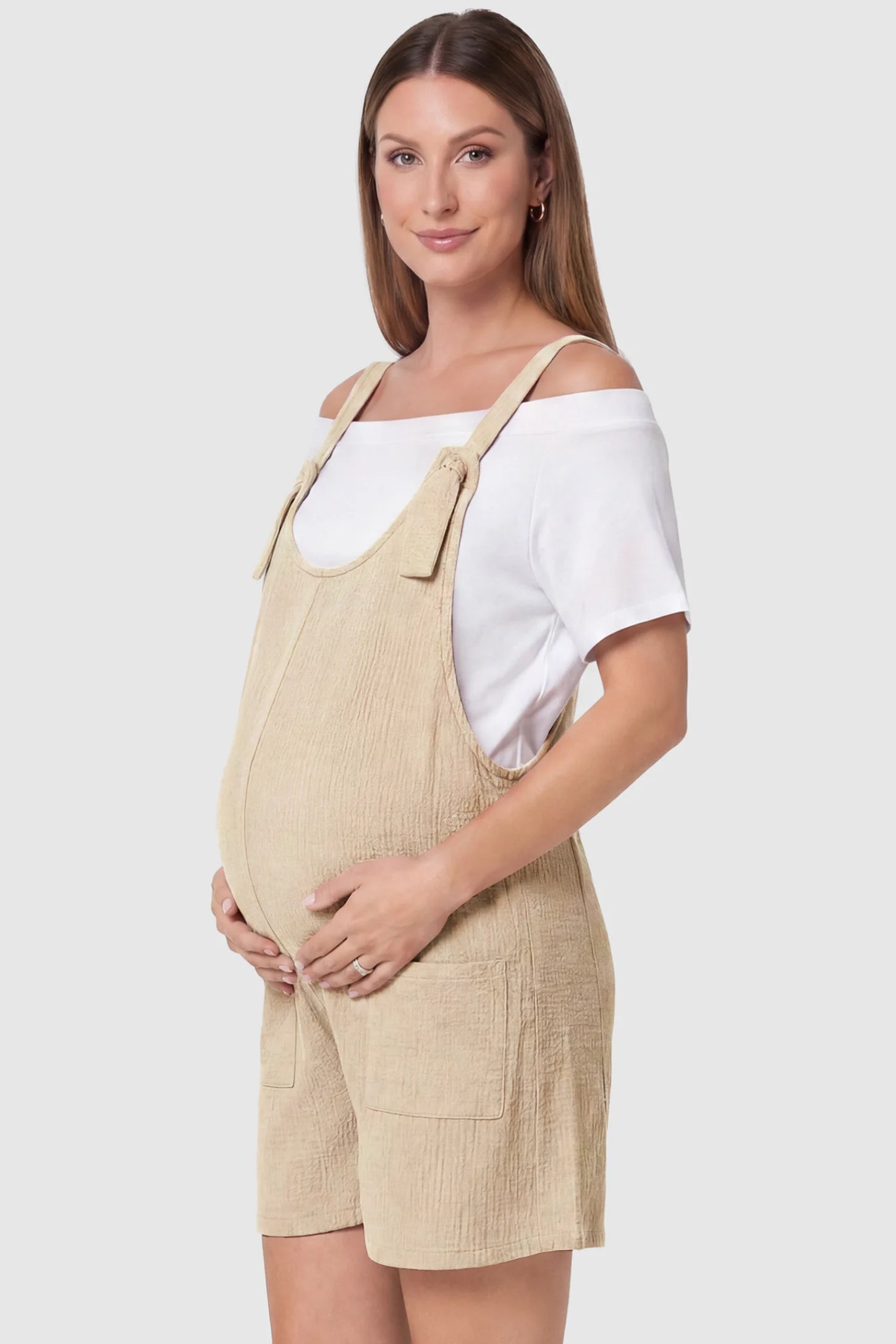 Knot Strap Front Pocket Maternity Romper Knot Strap Front Pocket Maternity Romper in Beige featuring deep front pockets and a scoop neck on a pregnant model, side view.