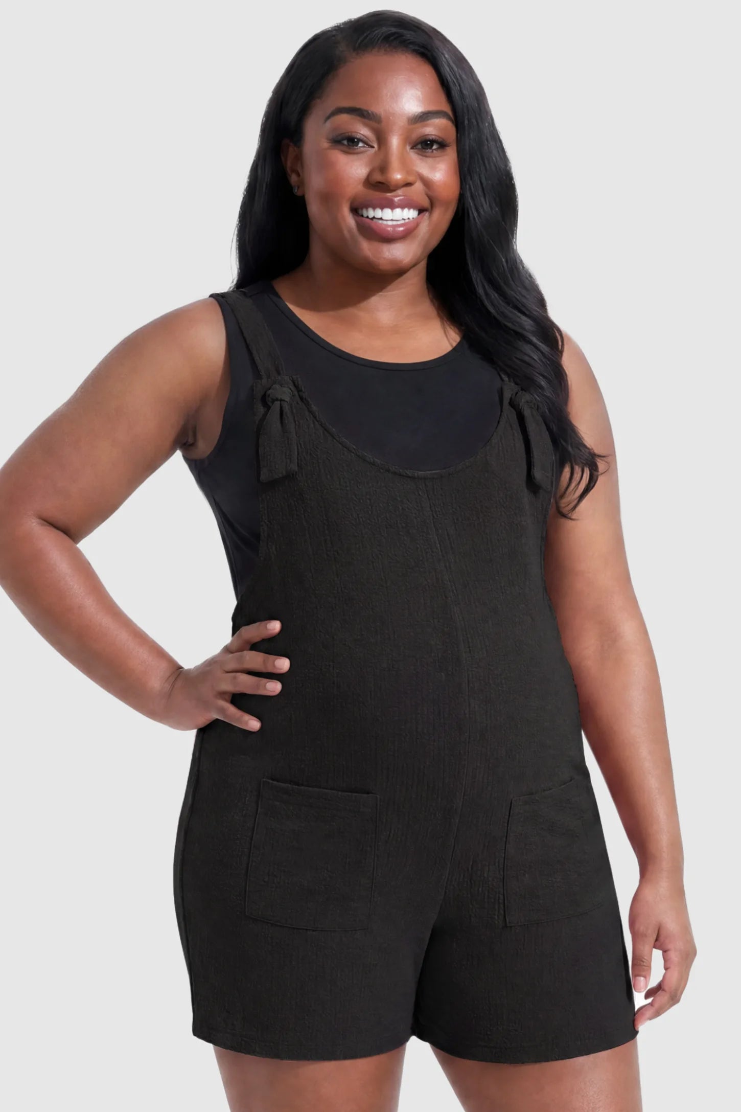 Knot Strap Front Pocket Maternity Romper Knot Strap Front Pocket Maternity Romper in Black featuring deep front pockets and a scoop neck on a plus size pregnant model, front view.