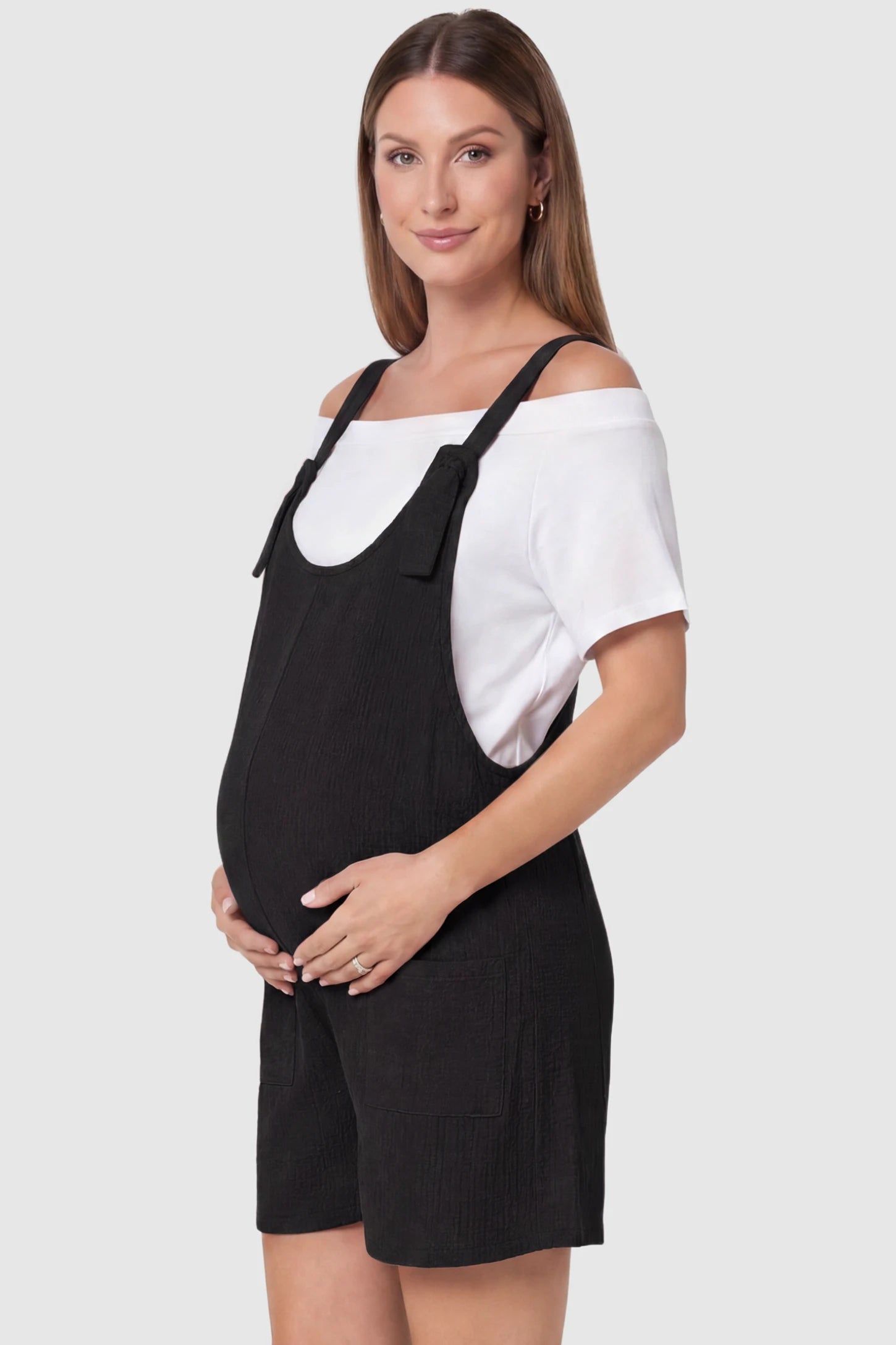 Knot Strap Front Pocket Maternity Romper Knot Strap Front Pocket Maternity Romper in Black featuring deep front pockets and a scoop neck on a pregnant model, side view.