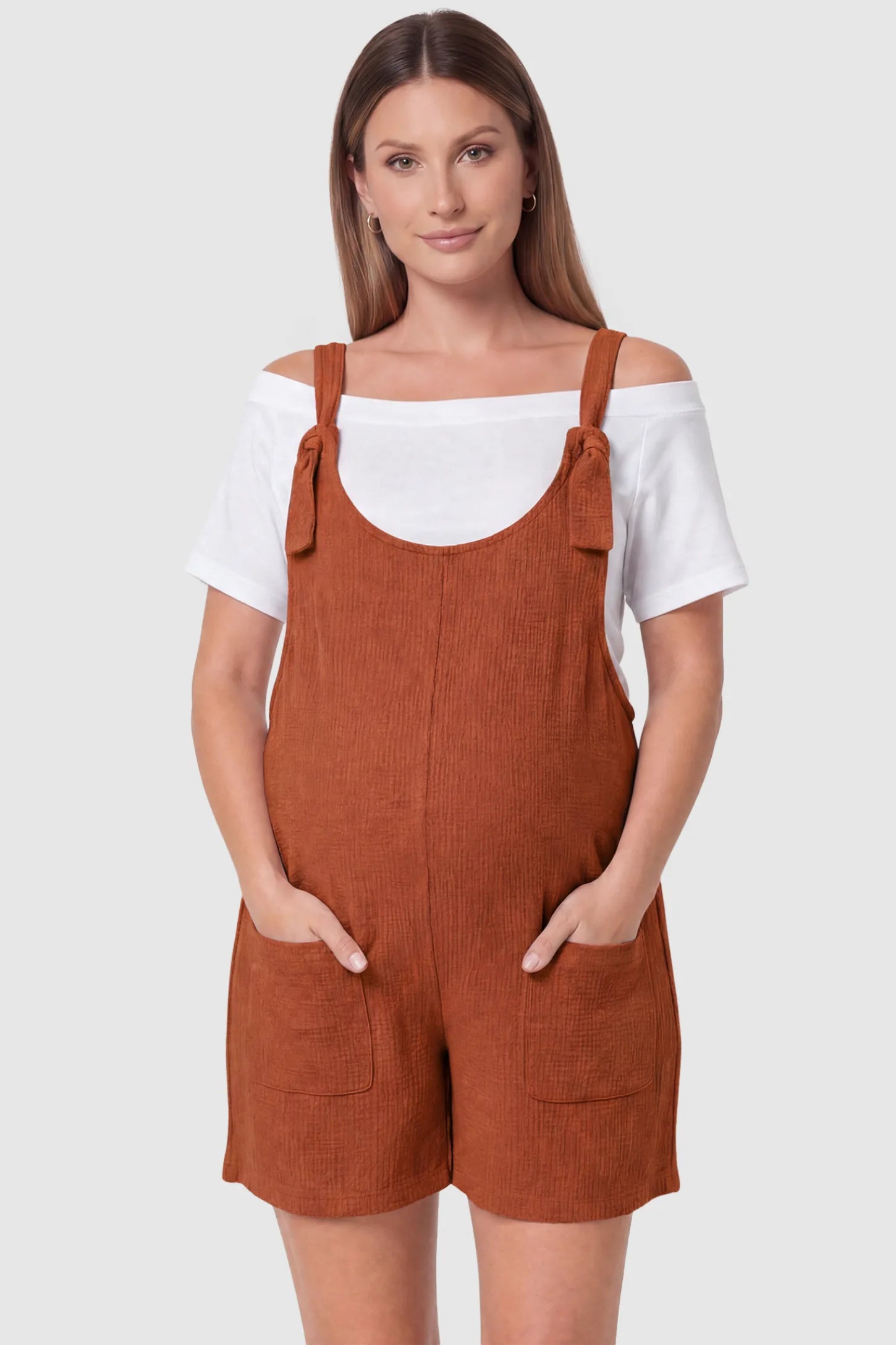 Knot Strap Front Pocket Maternity Romper Knot Strap Front Pocket Maternity Romper in Dark Brown featuring deep front pockets and a scoop neck on a pregnant model, front view.