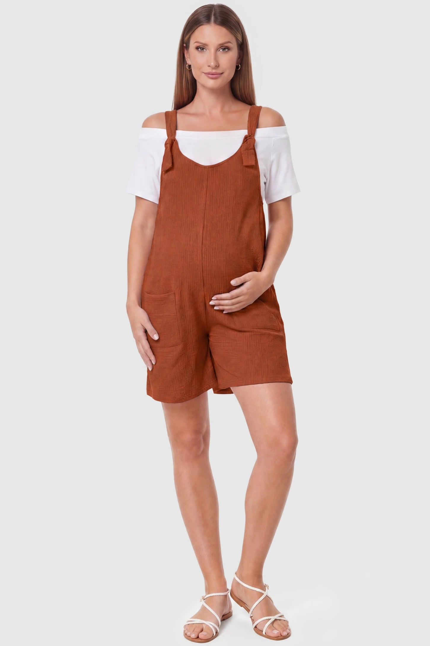 Knot Strap Front Pocket Maternity Romper Knot Strap Front Pocket Maternity Romper in Dark Brown featuring deep front pockets and a scoop neck on a pregnant model, full body view.