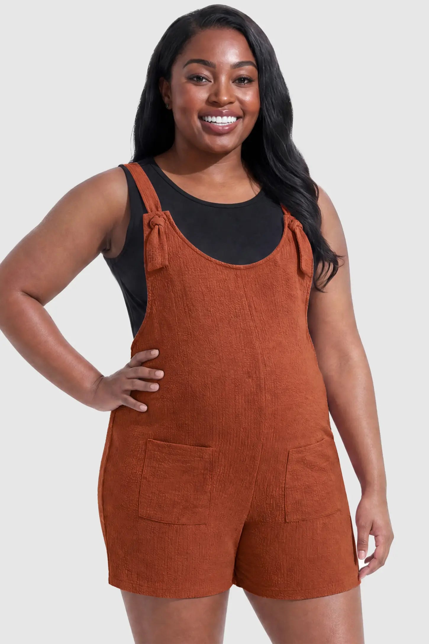 Knot Strap Front Pocket Maternity Romper Knot Strap Front Pocket Maternity Romper in Dark Brown featuring deep front pockets and a scoop neck on a plus size pregnant model, front view.