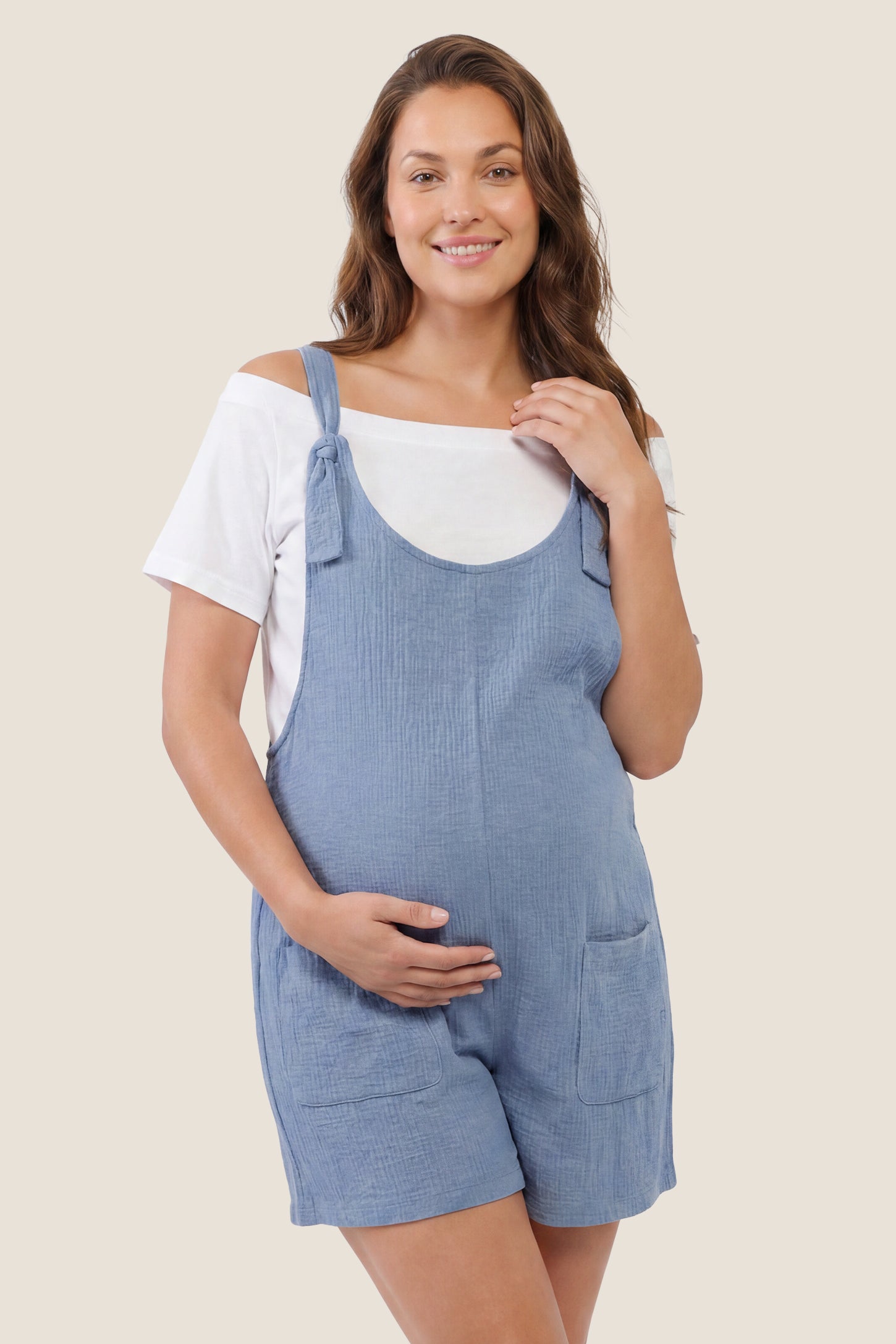 Knot Strap Front Pocket Maternity Romper Knot Strap Front Pocket Maternity Romper in Light Blue featuring deep front pockets and a scoop neck on a pregnant model, front view.
