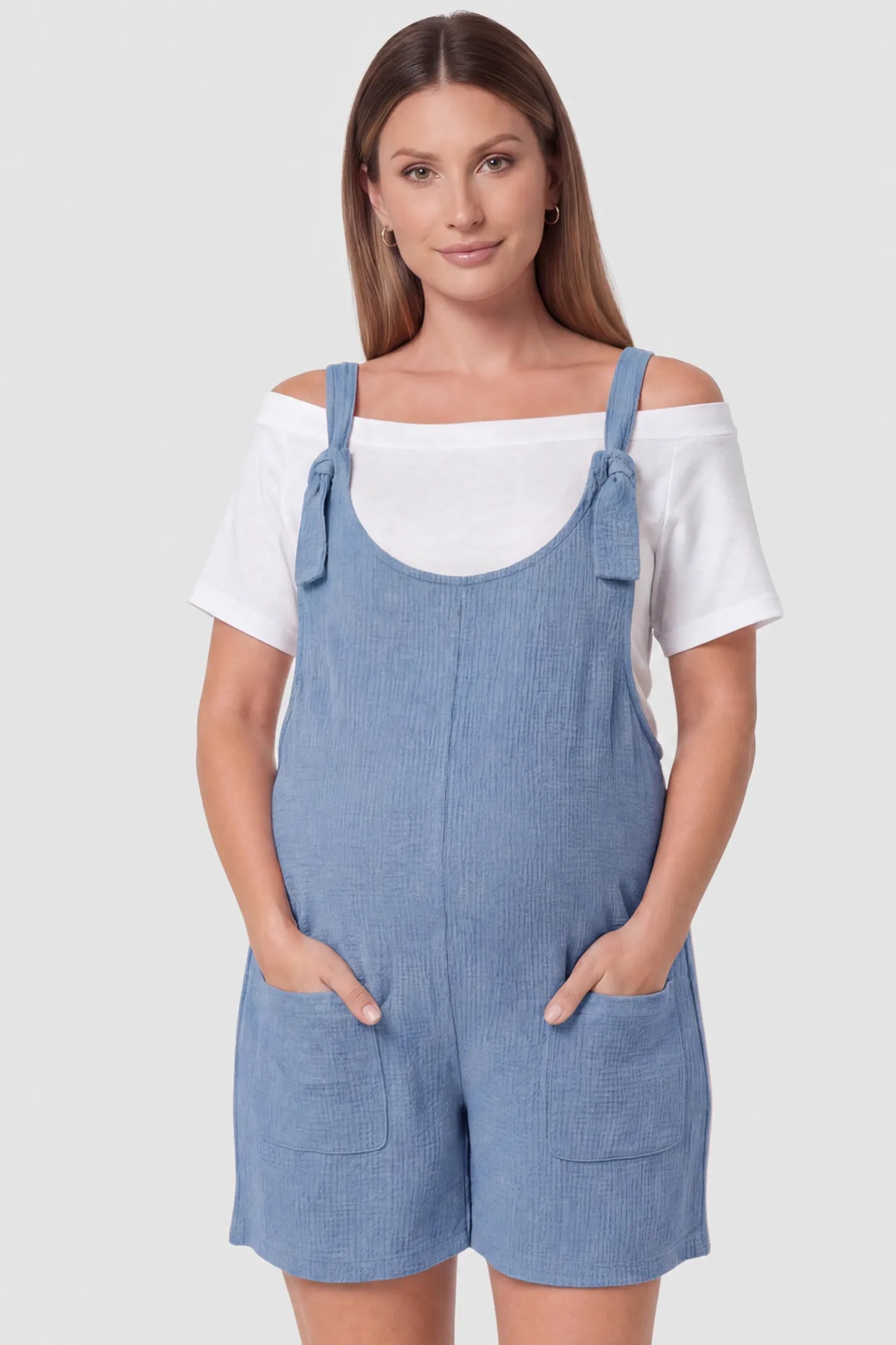 Knot Strap Front Pocket Maternity Romper Knot Strap Front Pocket Maternity Romper in Light Blue featuring deep front pockets and a scoop neck on a pregnant model, front view.