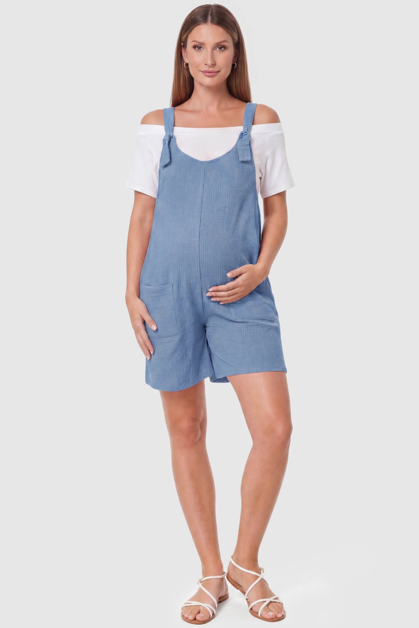 Knot Strap Front Pocket Maternity Romper Knot Strap Front Pocket Maternity Romper in Light Blue featuring deep front pockets and a scoop neck on a pregnant model, full body view.