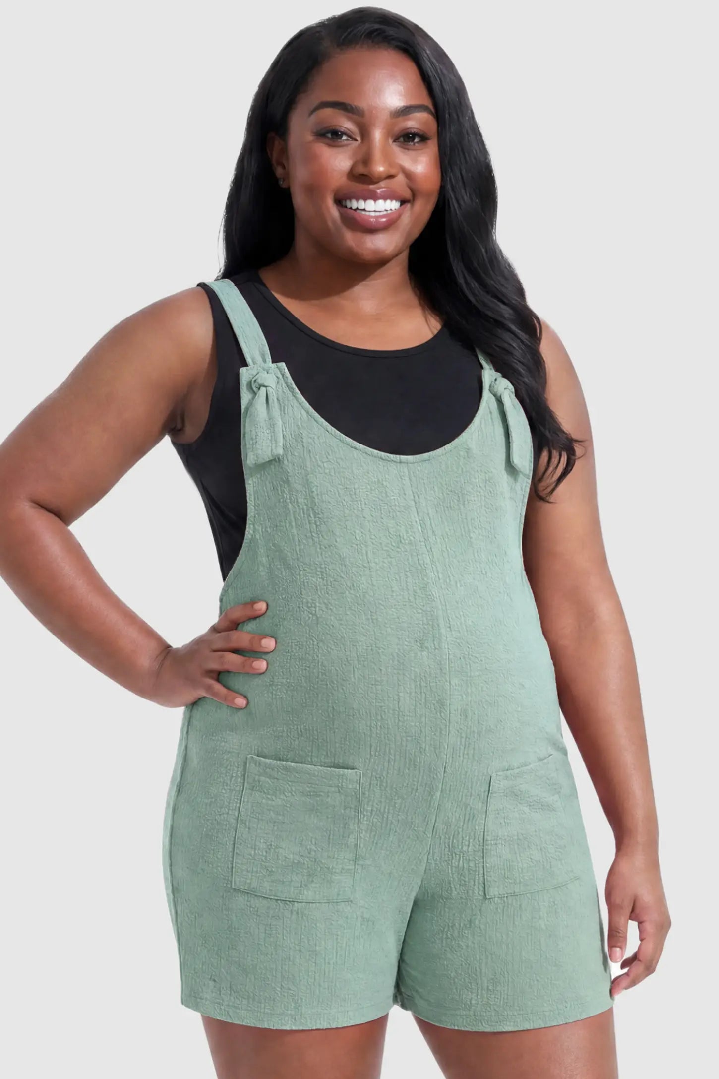 Knot Strap Front Pocket Maternity Romper Knot Strap Front Pocket Maternity Romper in Light Green featuring deep front pockets and a scoop neck on a plus size pregnant model, front view.