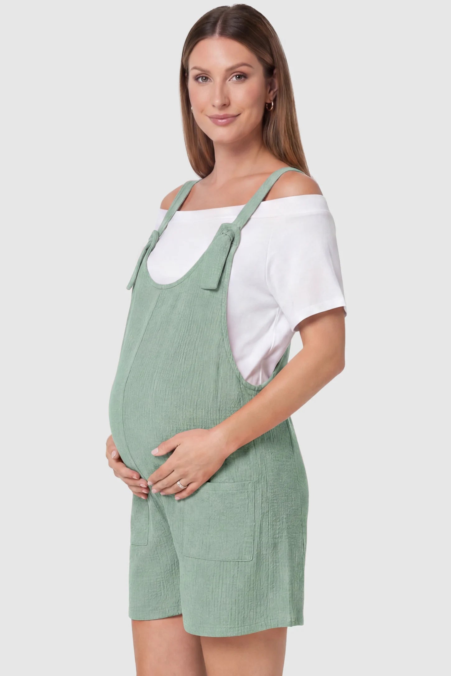 Knot Strap Front Pocket Maternity Romper Knot Strap Front Pocket Maternity Romper in Light Green featuring deep front pockets and a scoop neck on a pregnant model, side view.