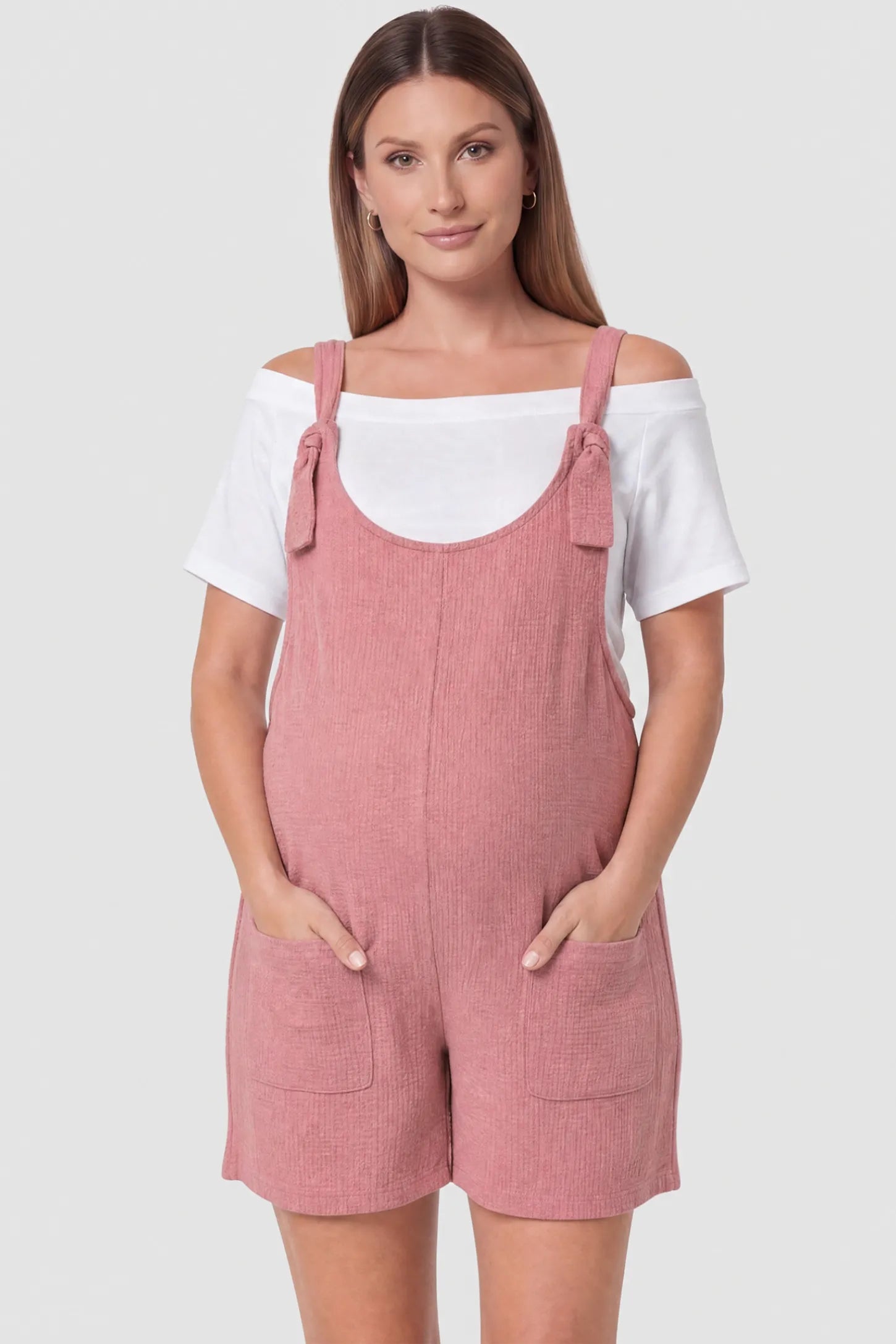 Knot Strap Front Pocket Maternity Romper Knot Strap Front Pocket Maternity Romper in Pink featuring deep front pockets and a scoop neck on a pregnant model, front view.