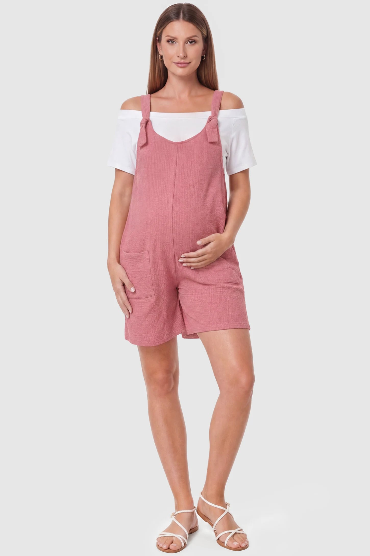Knot Strap Front Pocket Maternity Romper Knot Strap Front Pocket Maternity Romper in Pink featuring deep front pockets and a scoop neck on a pregnant model, full body view.