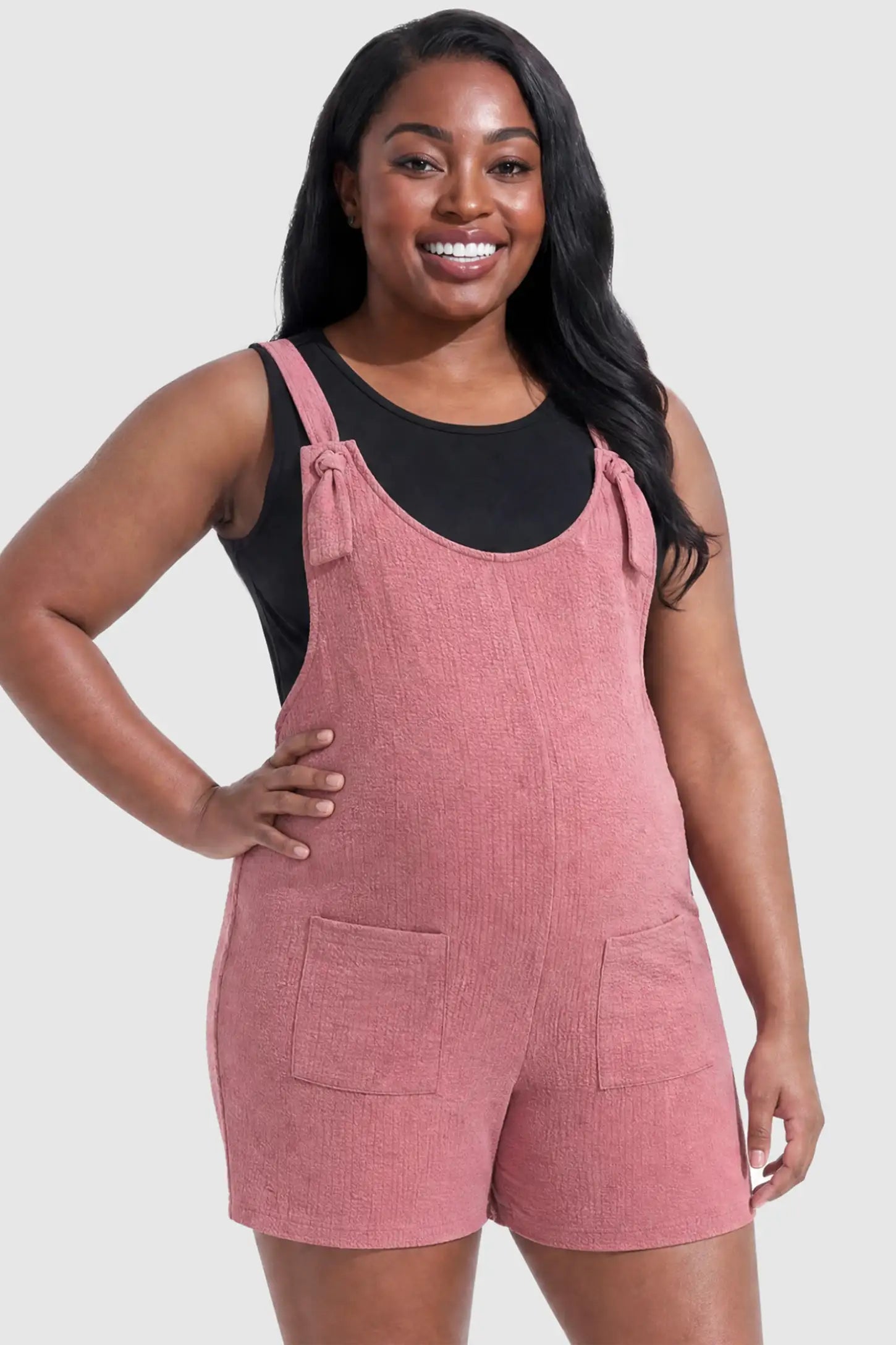 Knot Strap Front Pocket Maternity Romper Knot Strap Front Pocket Maternity Romper in Pink featuring deep front pockets and a scoop neck on a plus size pregnant model, front view.