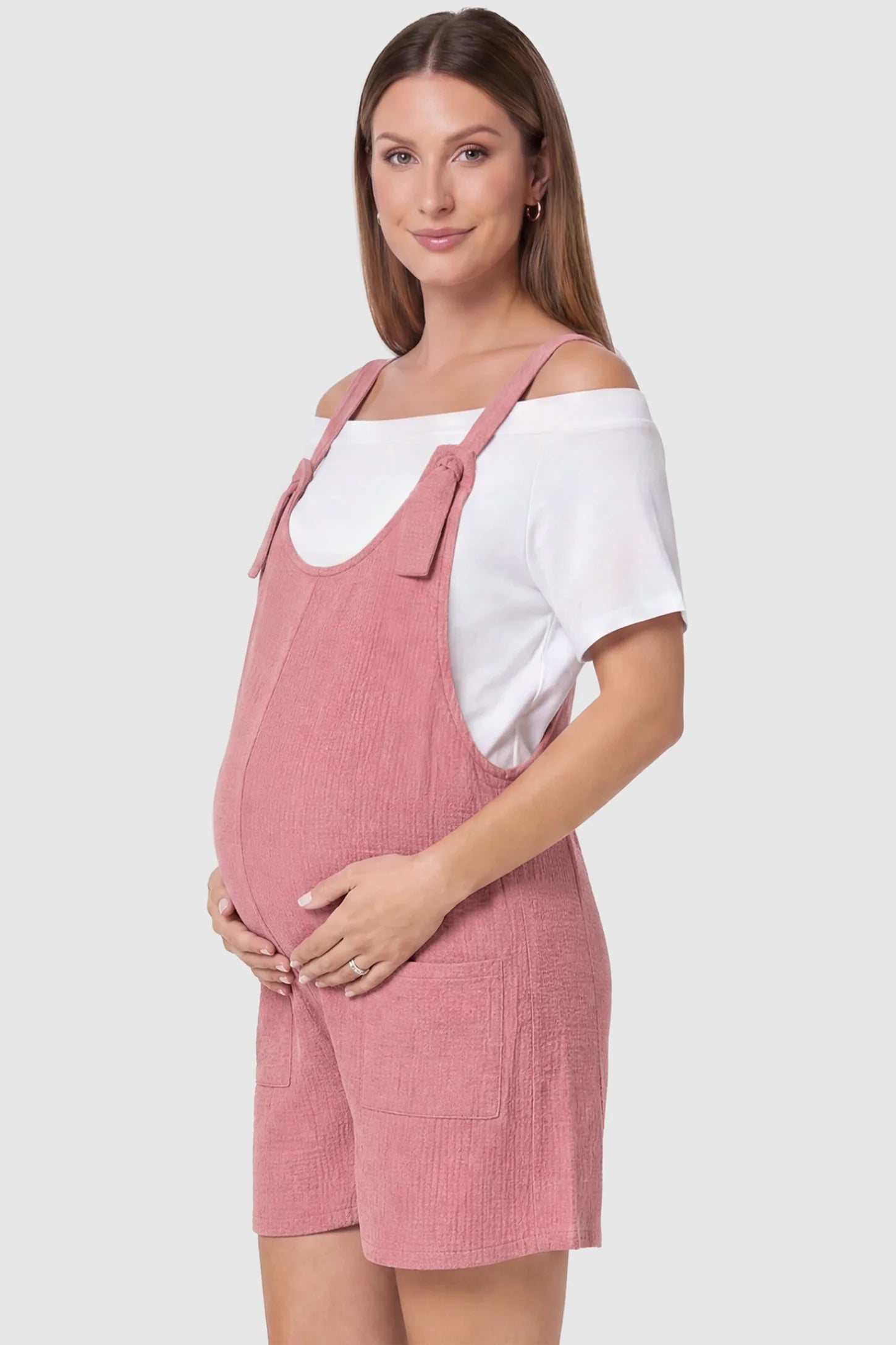 Knot Strap Front Pocket Maternity Romper Knot Strap Front Pocket Maternity Romper in Pink featuring deep front pockets and a scoop neck on a pregnant model, side view.