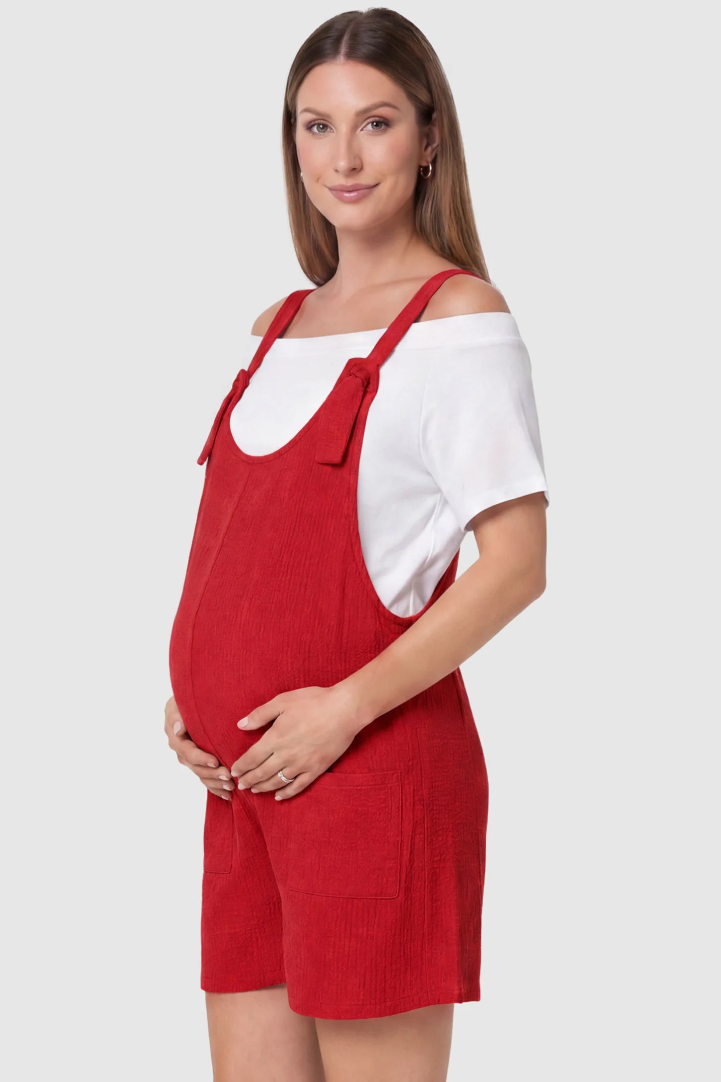 Knot Strap Front Pocket Maternity Romper Knot Strap Front Pocket Maternity Romper in Red featuring deep front pockets and a scoop neck on a pregnant model, side view.