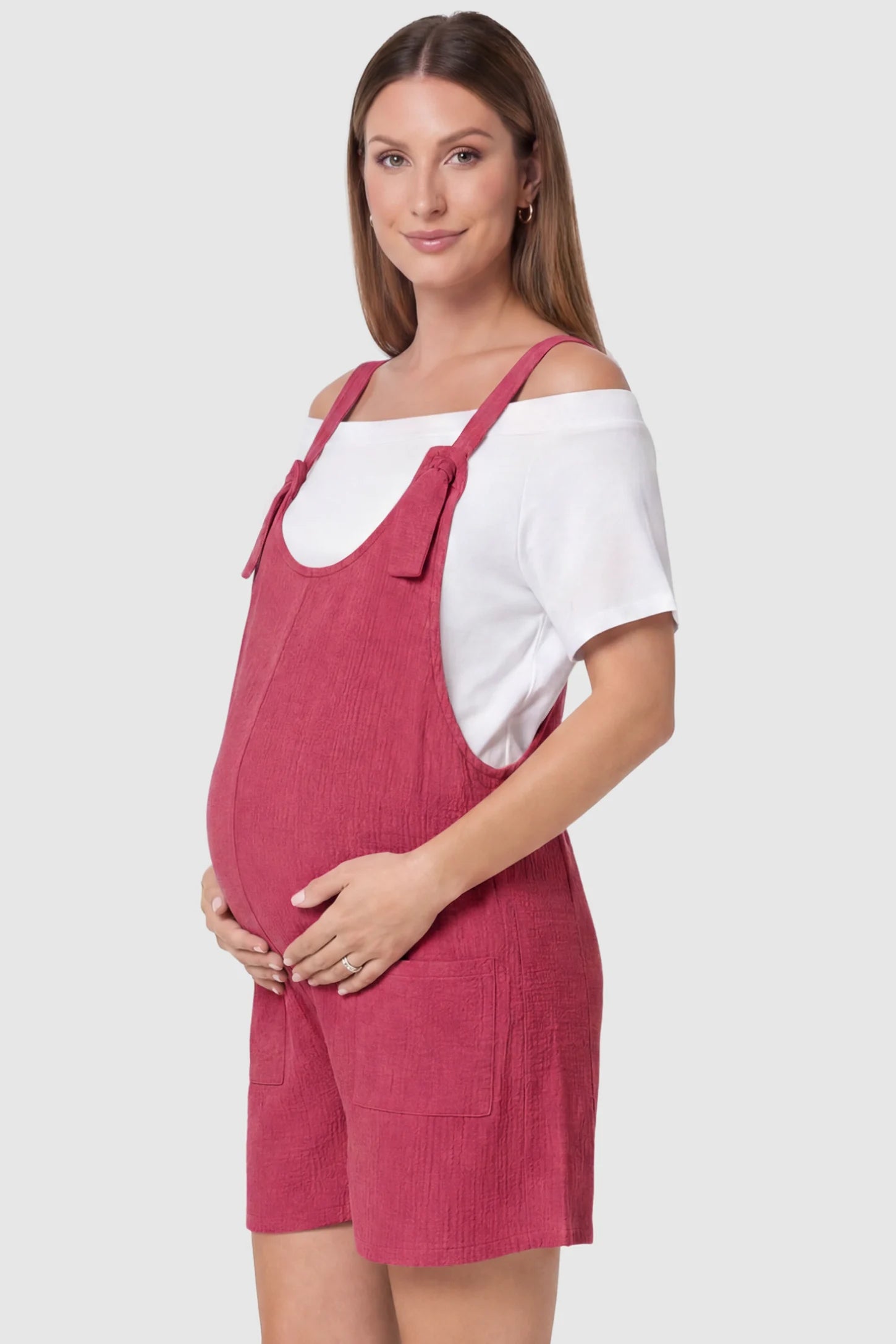 Knot Strap Front Pocket Maternity Romper Knot Strap Front Pocket Maternity Romper in Rose Red featuring deep front pockets and a scoop neck on a pregnant model, side view.
