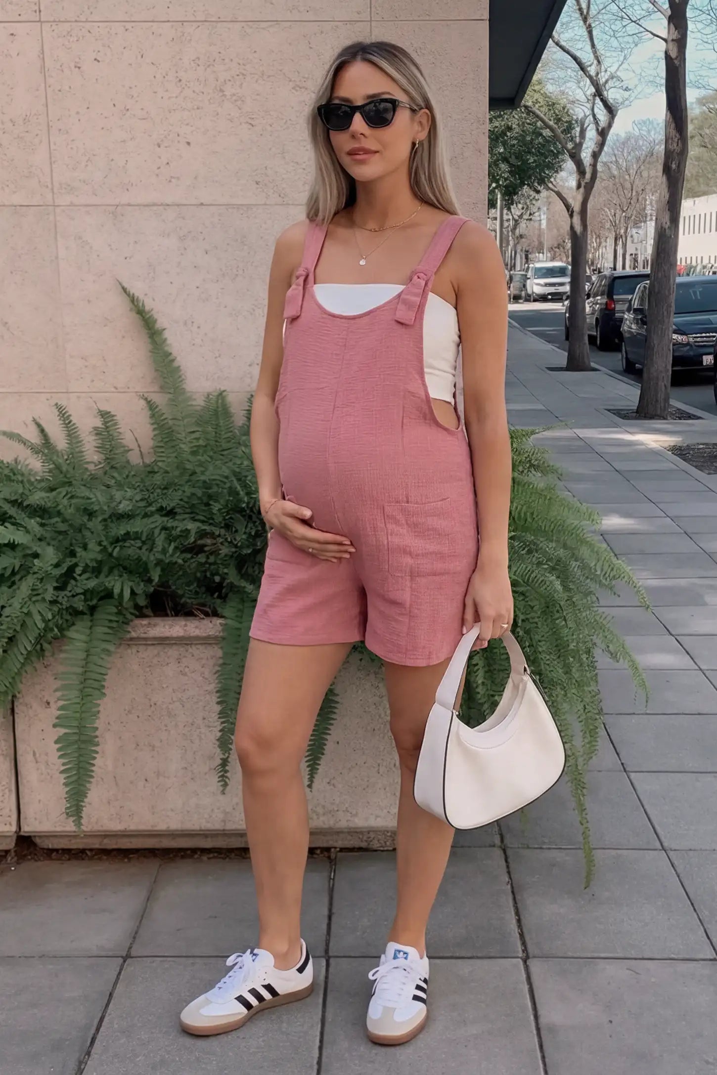 Knot Strap Front Pocket Maternity Romper Outdoor lifestyle image of the pink Knot Strap Front Pocket Maternity Romper styled with sneakers and a shoulder bag.