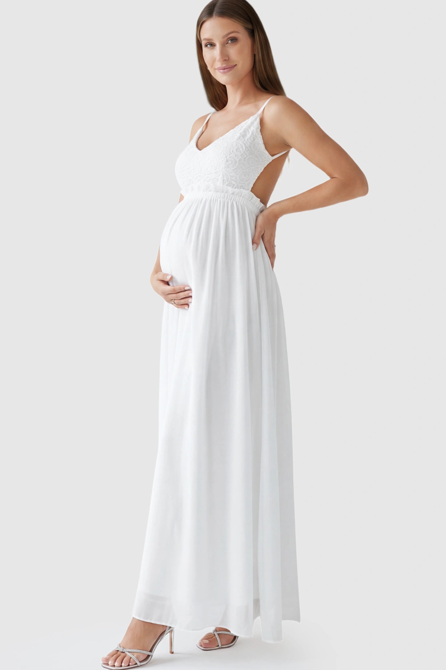 Lace Bodice V-Neck Maternity Maxi Dress Lace Bodice V-Neck Maternity Maxi Dress in White featuring a floral lace overlay and spaghetti straps on a pregnant model showing side.