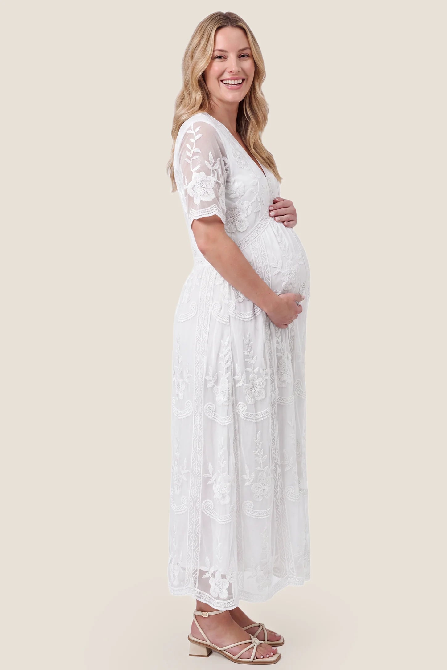 Lace Short Sheer Sleeve Maternity Maxi Dress Lace Short Sheer Sleeve Maternity Maxi Dress in white featuring floral lace detail on a pregnant model, side view.