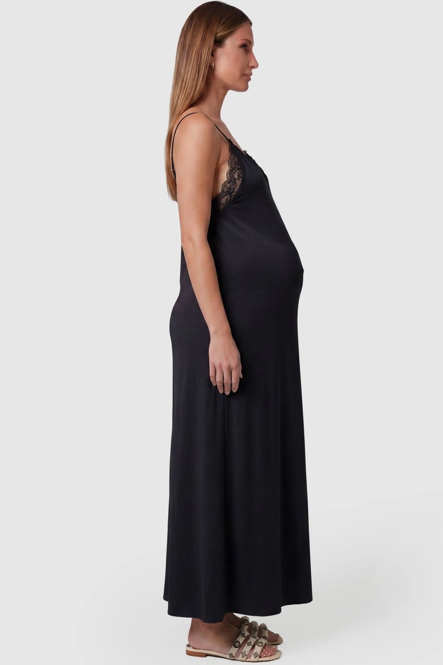 Lace-Trim Maternity Slip Dress Lace-Trim Maternity Slip Dress in Black featuring dainty spaghetti straps on a pregnant model, side view.