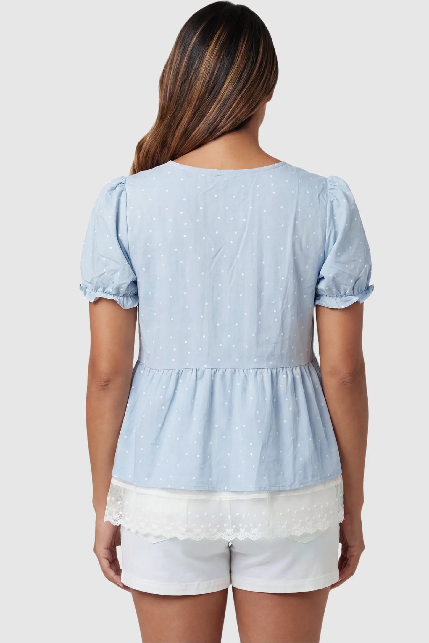 Laced Polka Dot Babydoll Maternity Blouse Laced Polka Dot Babydoll Maternity Blouse in Blue featuring a tiered peplum silhouette on a pregnant model, back view.