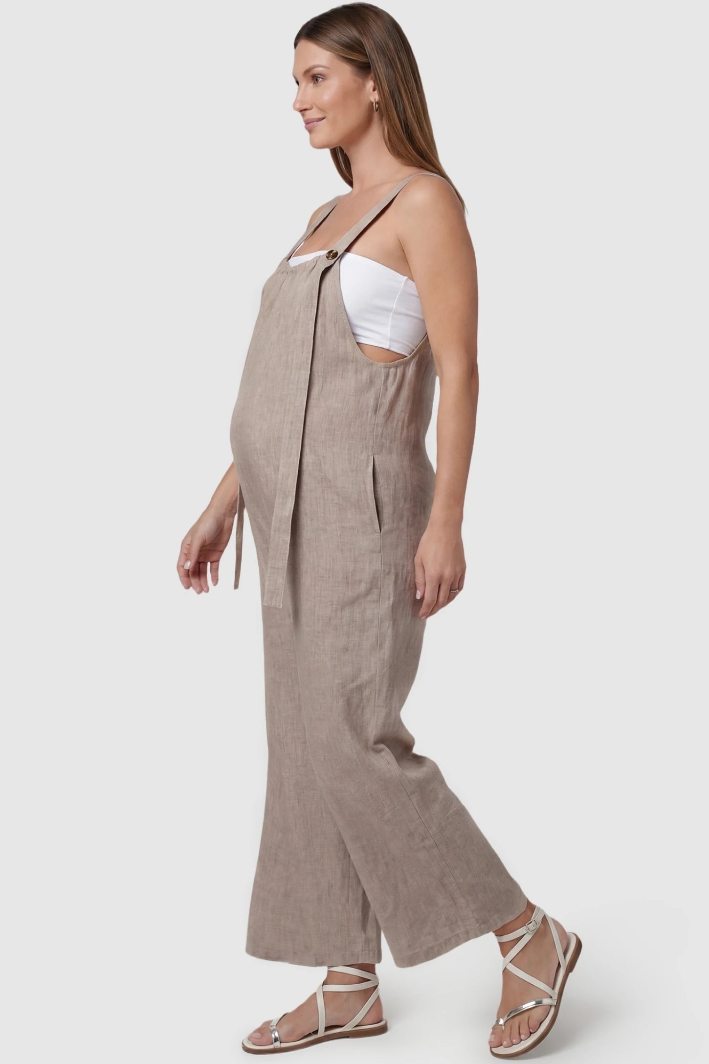 Loose Fit Wide Leg Sleeveless Maternity Jumpsuit Loose Fit Wide Leg Sleeveless Maternity Jumpsuit in Light Brown featuring an open side panel and flowing wide leg on a pregnant model, side view.
