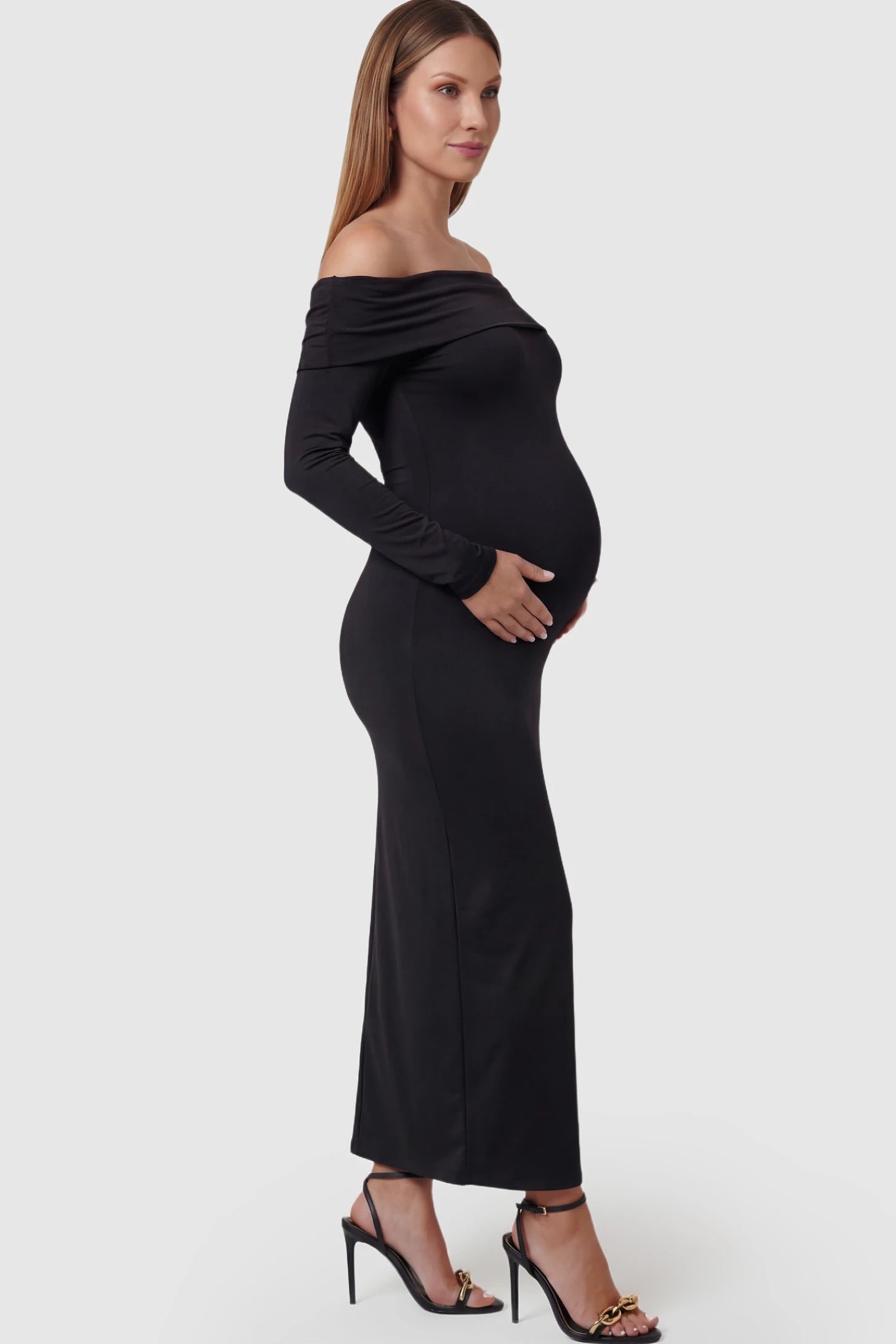 Solid Off Shoulder Bodycon Maternity Maxi Dress Off Shoulder Bodycon Maternity Maxi Dress in black featuring a smooth stretch finish on a pregnant model showing side.
