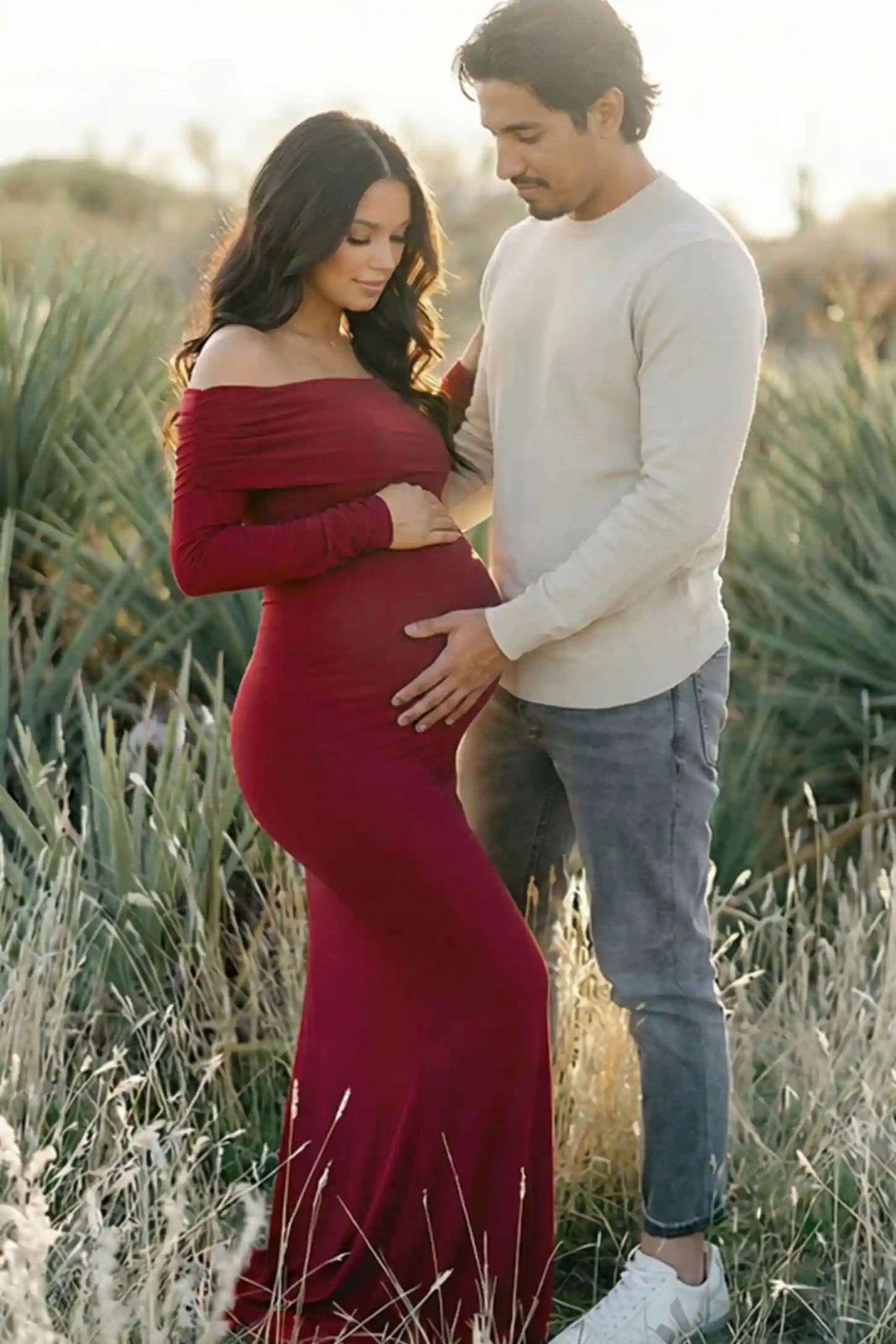 Solid Off Shoulder Bodycon Maternity Maxi Dress Off Shoulder Bodycon Maternity Maxi Dress in Red featuring a smooth stretch finish on a pregnant model posing with a partner.