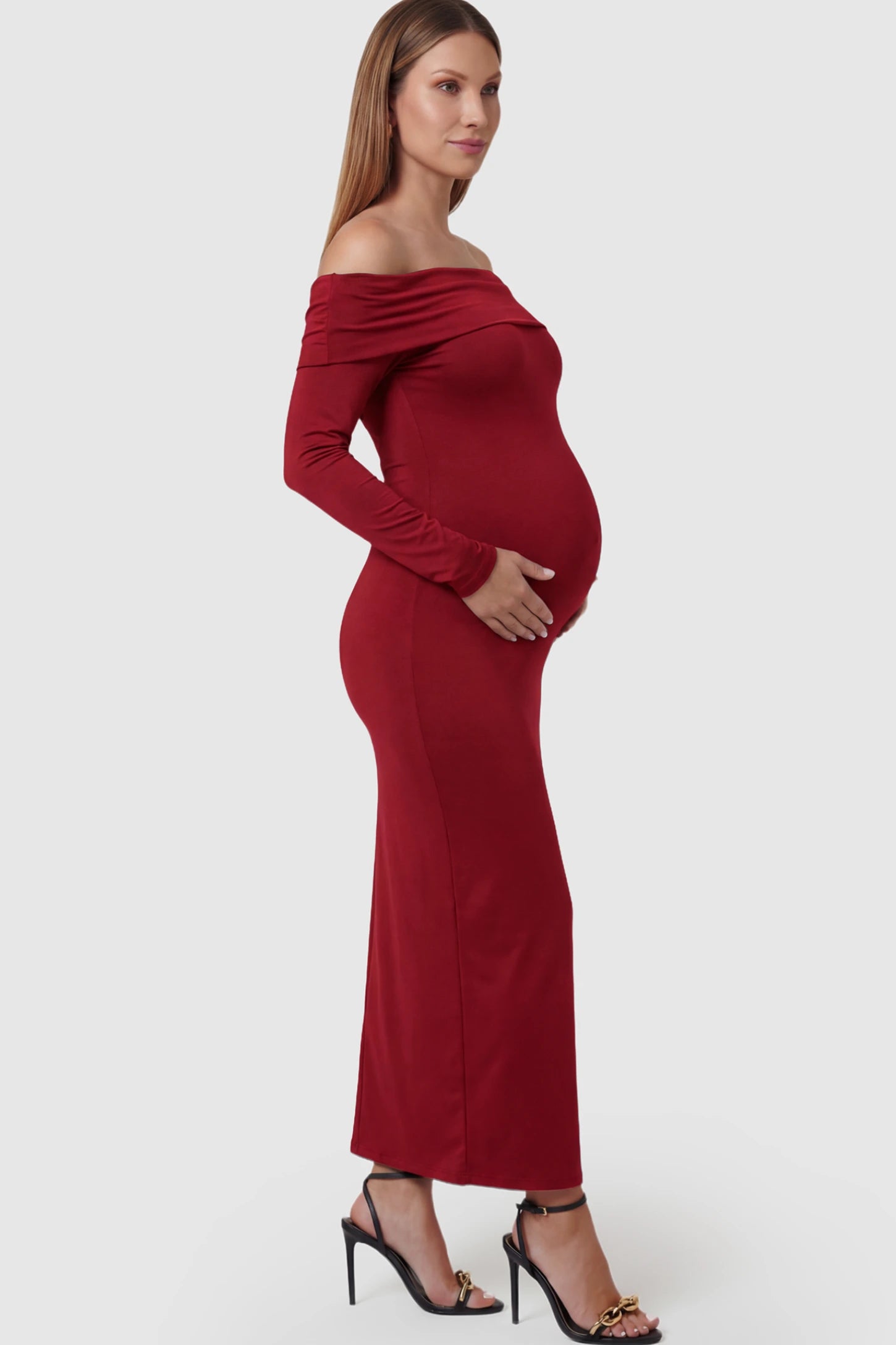 Solid Off Shoulder Bodycon Maternity Maxi Dress Off Shoulder Bodycon Maternity Maxi Dress in red featuring a smooth stretch finish on a pregnant model showing side.