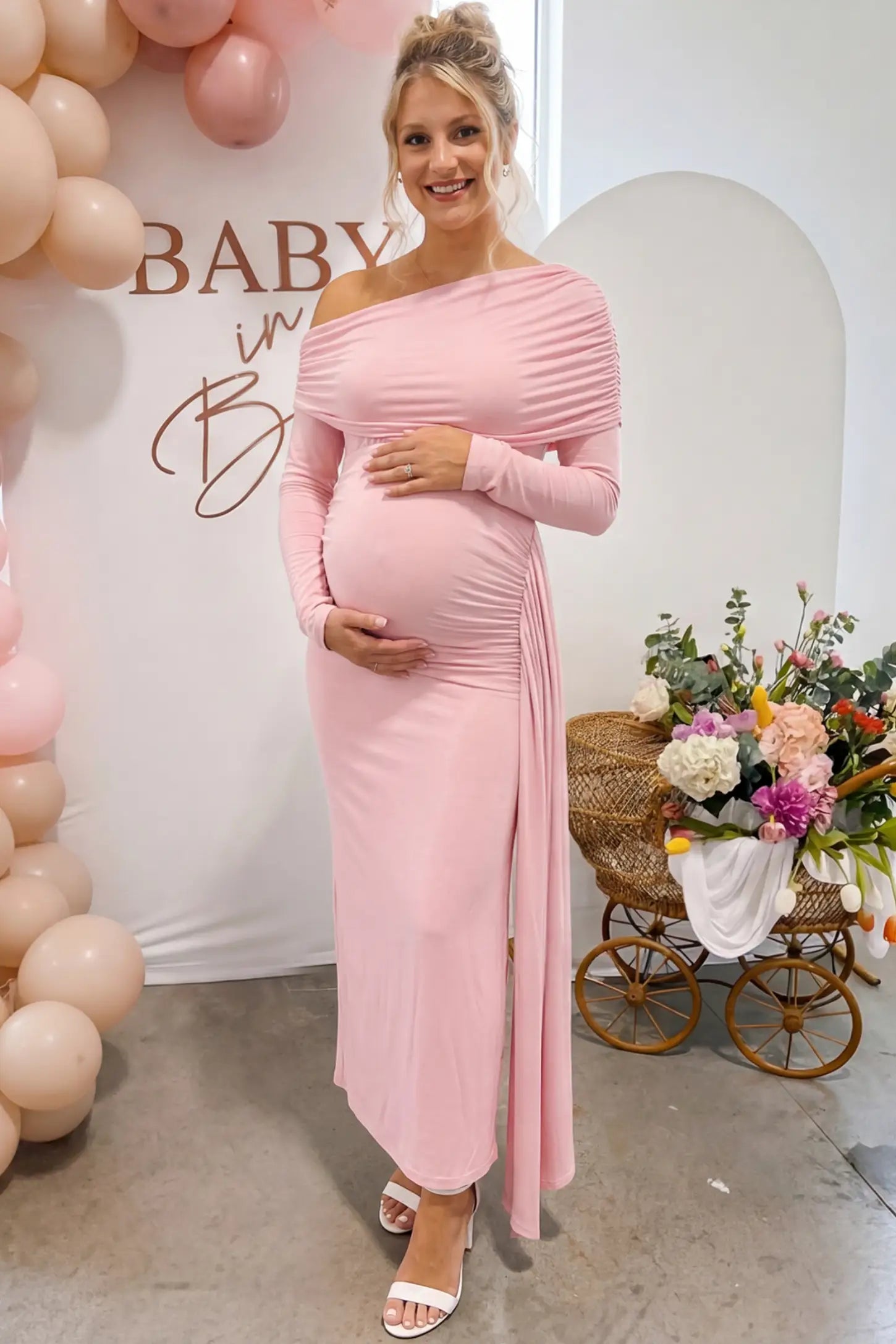 Off Shoulder Draped Wrap Bodycon Maternity Maxi Dress in Pink featuring side ruching and long sleeves on a pregnant woman in an outdoor setting front view.