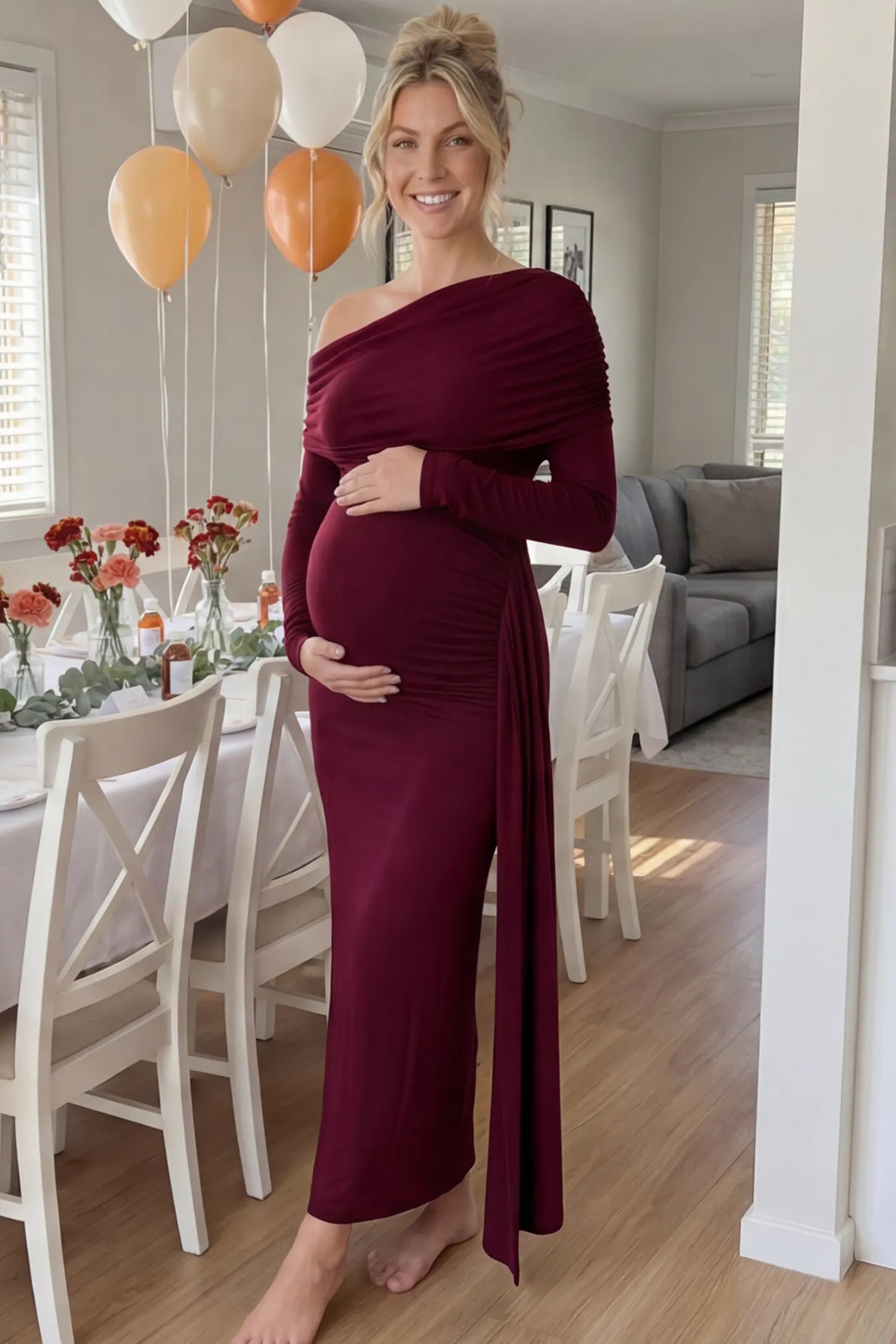 Off Shoulder Draped Wrap Bodycon Maternity Maxi Dress Off Shoulder Draped Wrap Bodycon Maternity Maxi Dress in Wine Red featuring side ruching and long sleeves on a pregnant woman cradling her baby bump at a baby shower, front view.