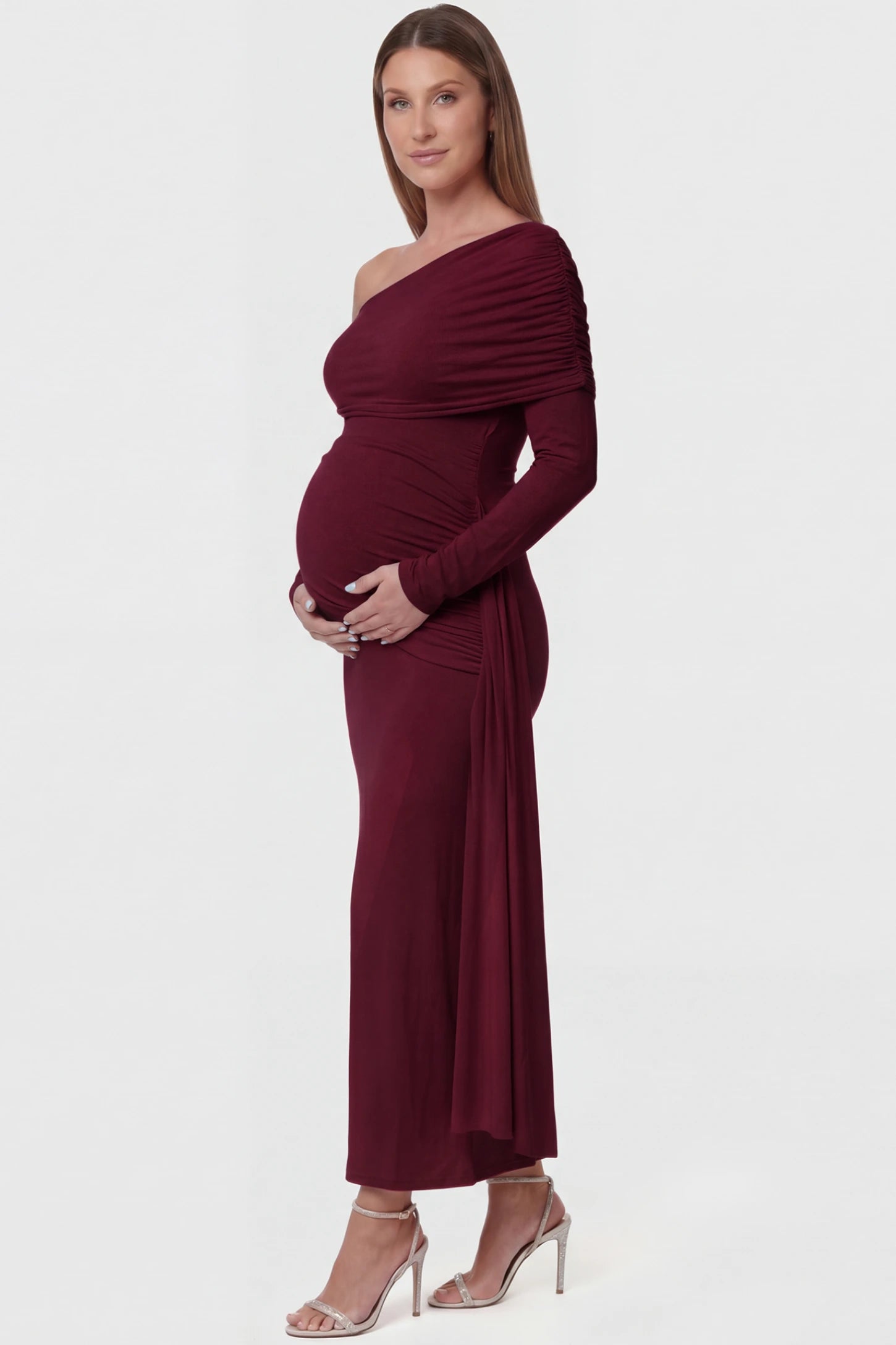 Off Shoulder Draped Wrap Bodycon Maternity Maxi Dress Off Shoulder Draped Wrap Bodycon Maternity Maxi Dress in Wine Red featuring side ruching and long sleeves on a pregnant model side view.