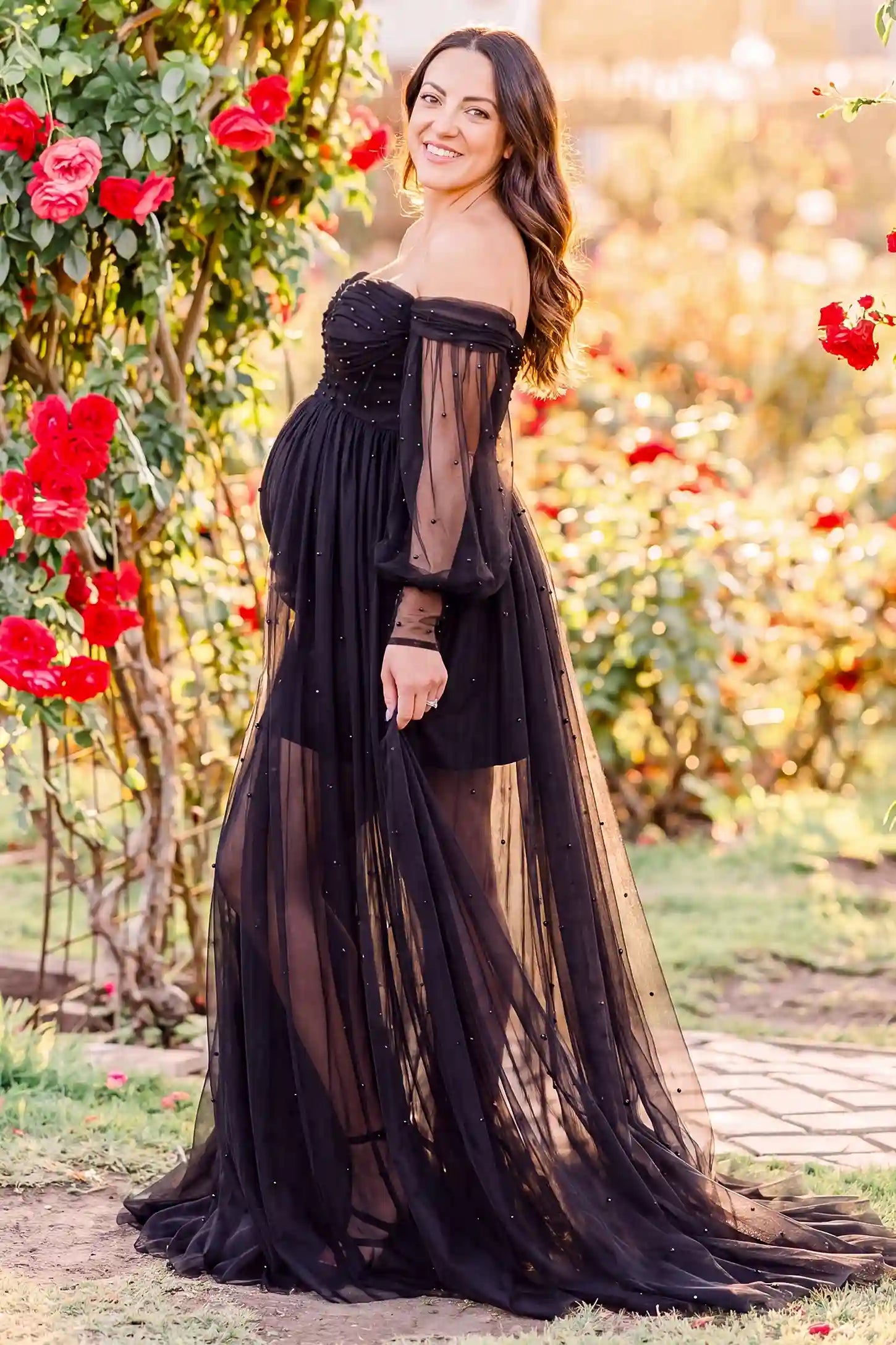 Off-Shoulder Empire Waist Tulle Maternity Gown Off-Shoulder Empire Waist Maternity Gown in Black highlighting the empire waist, outdoor lifestyle side view on a pregnant model.