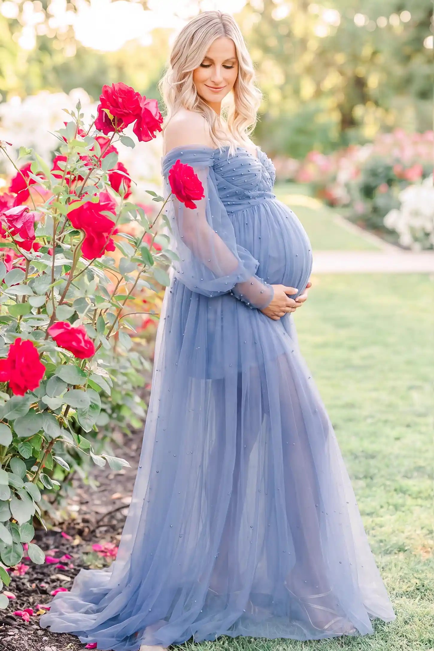 Off-Shoulder Empire Waist Tulle Maternity Gown Off-Shoulder Empire Waist Maternity Gown in Blue with a flowing A-line shape, outdoor lifestyle view on a pregnant model.
