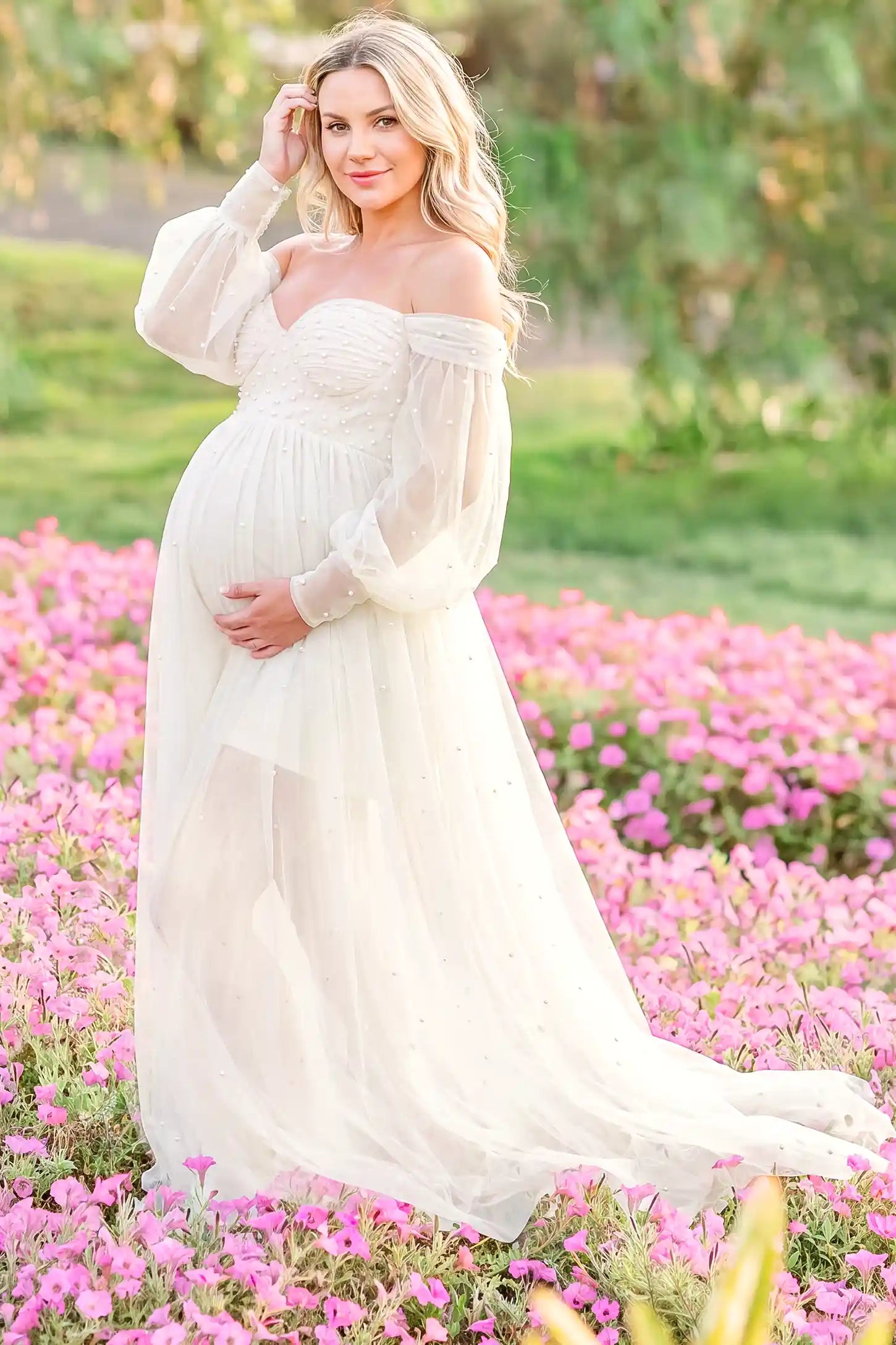 Off-Shoulder Empire Waist Tulle Maternity Gown Off-Shoulder Empire Waist Maternity Gown in Ivory featuring an off-shoulder sweetheart neckline, outdoor lifestyle front view on a pregnant model.