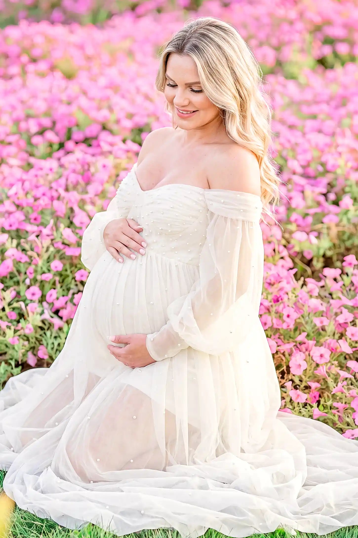 Off-Shoulder Empire Waist Tulle Maternity Gown Off-Shoulder Empire Waist Maternity Gown in Ivory featuring an off-shoulder sweetheart neckline, outdoor lifestyle front view on a pregnant model.