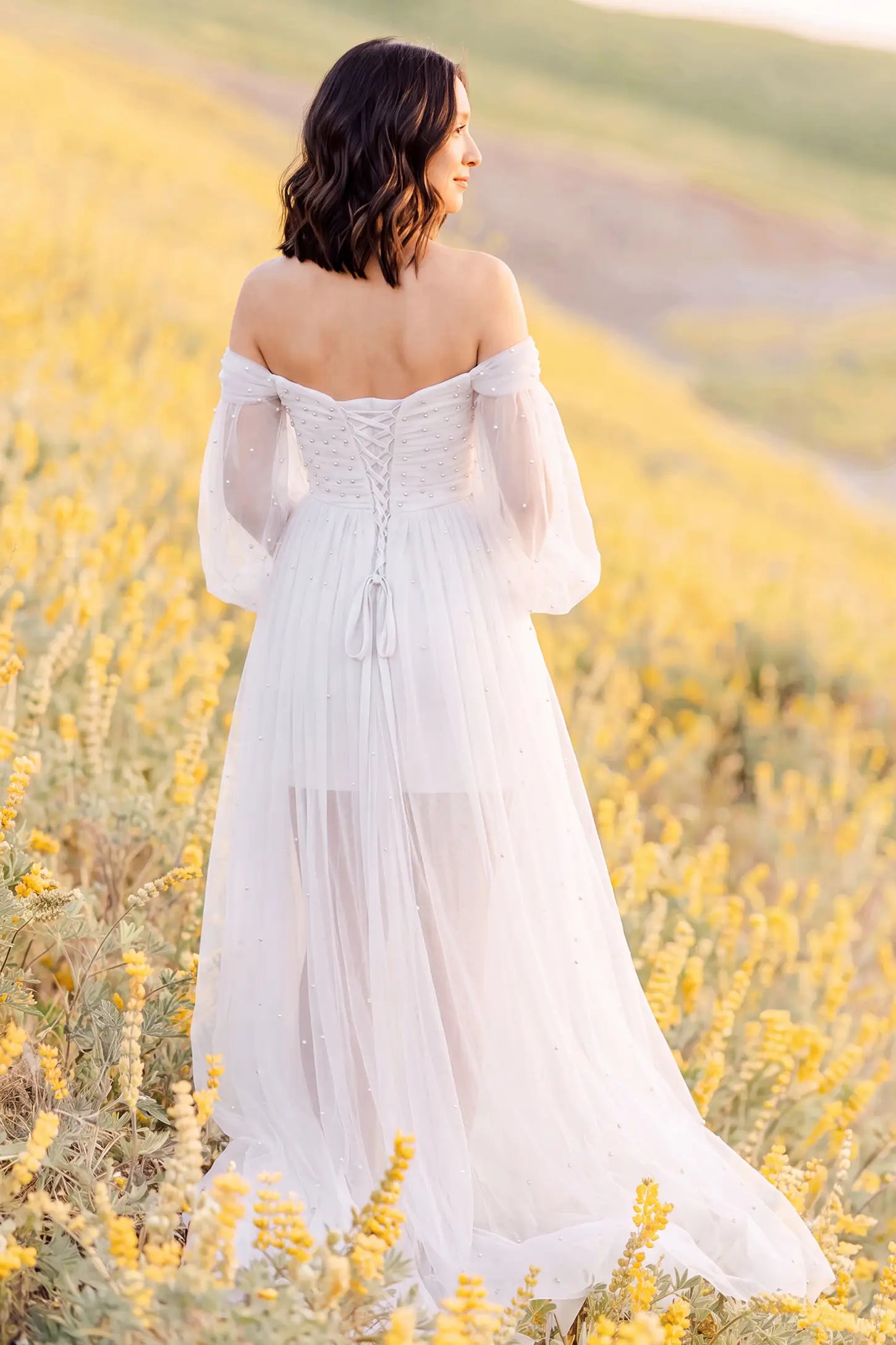 Off-Shoulder Empire Waist Tulle Maternity Gown Off-Shoulder Empire Waist Maternity Gown in White with a flowing A-line shape, outdoor lifestyle view on a pregnant model.