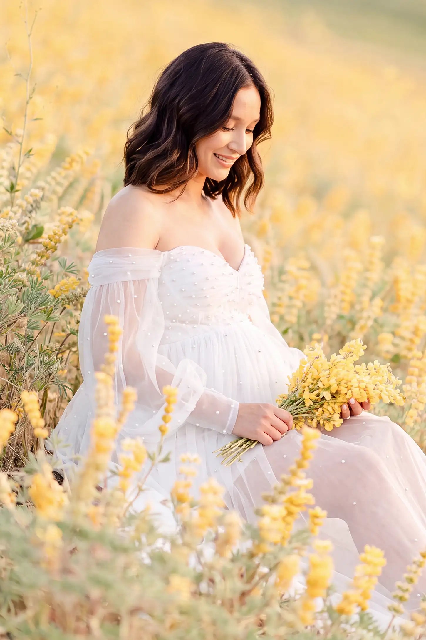 Off-Shoulder Empire Waist Tulle Maternity Gown Off-Shoulder Empire Waist Maternity Gown in White highlighting the empire waist, outdoor lifestyle side view on a pregnant model.