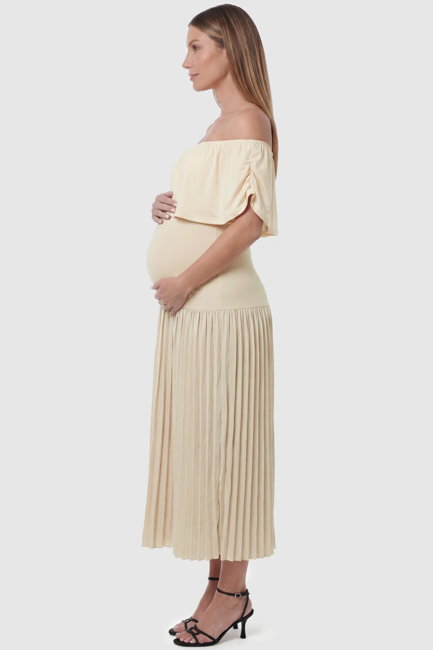 Pleated Off Shoulder Maternity Maxi Dress Pleated Off Shoulder Maternity Maxi Dress  in Beige featuring a high stretch pleated maxi skirt on a pregnant model, side view.