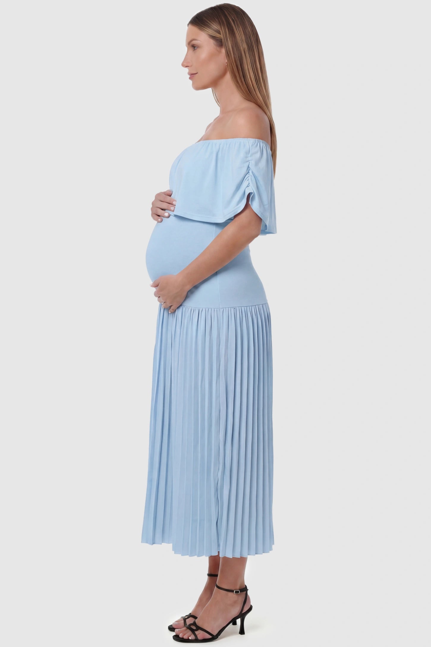 Pleated Off Shoulder Maternity Maxi Dress Pleated Off Shoulder Maternity Maxi Dress  in Light Blue featuring a high stretch pleated maxi skirt on a pregnant model, side view.
