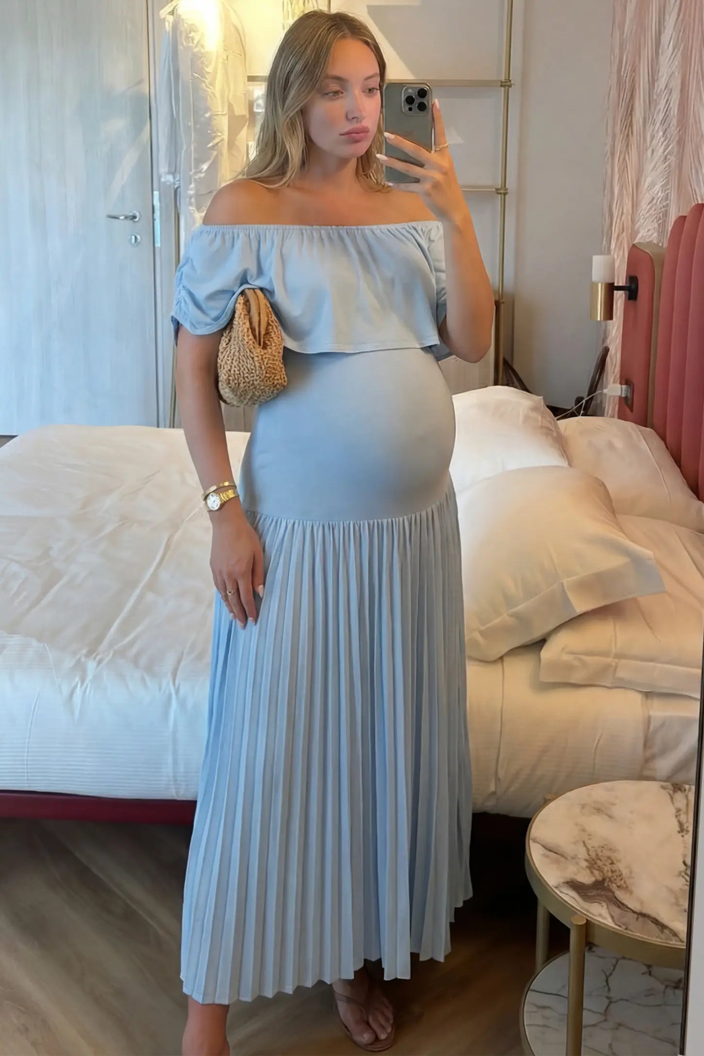 Pleated Off Shoulder Maternity Maxi Dress Pleated Off Shoulder Maternity Maxi Dress in Light Blue featuring a high stretch pleated maxi skirt on a pregnant model during an indoor setting, front view.