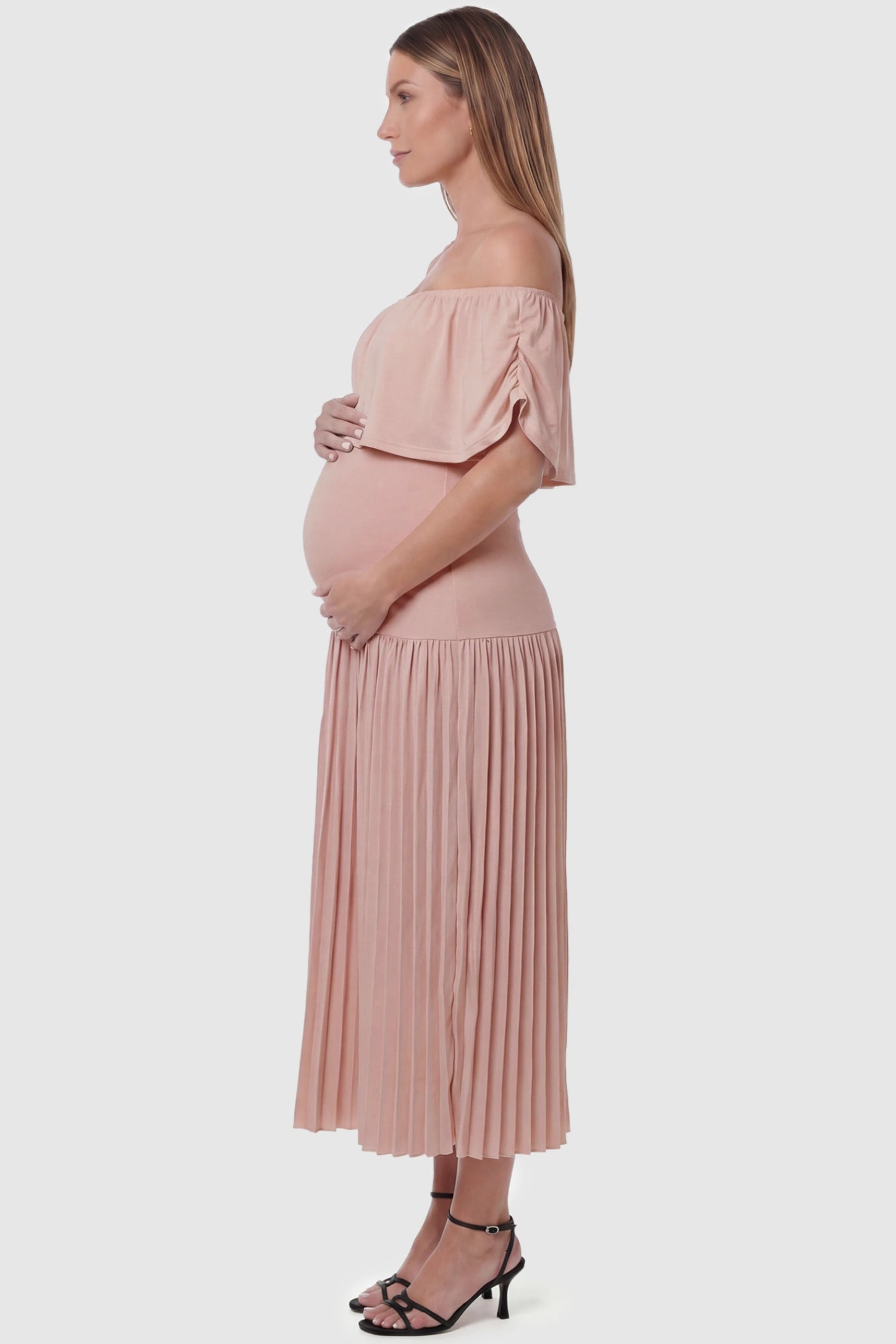 Pleated Off Shoulder Maternity Maxi Dress Pleated Off Shoulder Maternity Maxi Dress  in Pink featuring a high stretch pleated maxi skirt on a pregnant model, side view.