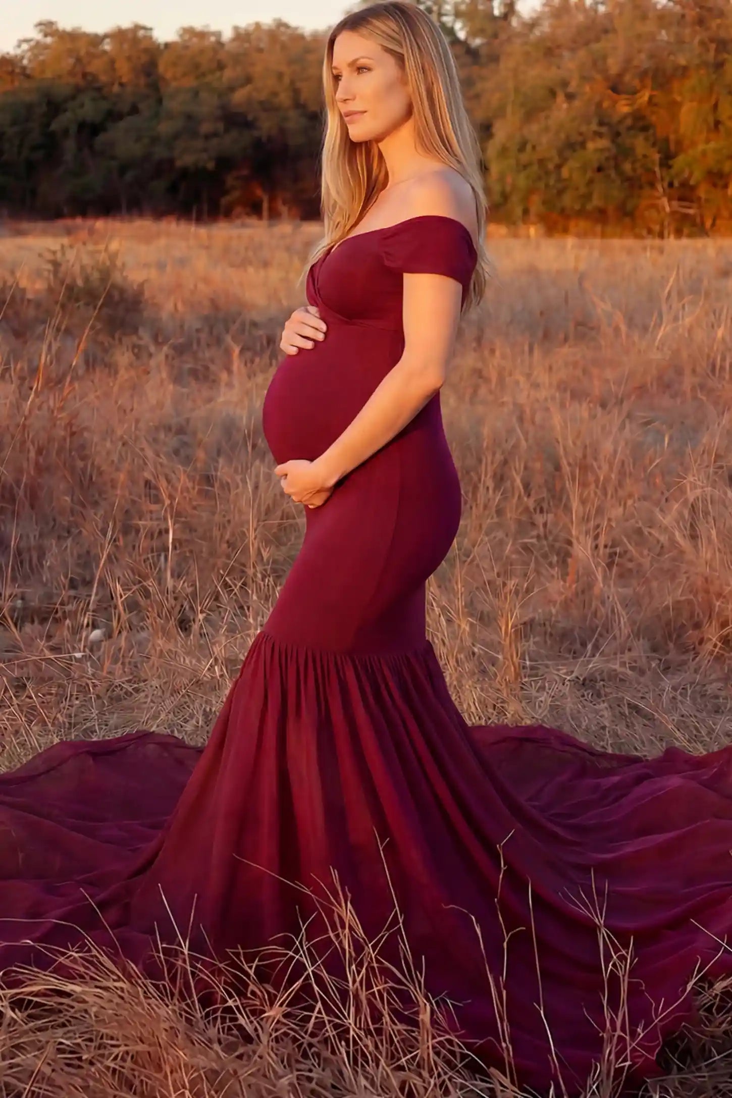 Solid Off Shoulder Mermaid Maternity Photoshoot Gown Solid Off Shoulder Mermaid Maternity Photoshoot Gown in burgundy featuring a sweetheart neckline and dramatic pleated train on a pregnant model showing side.