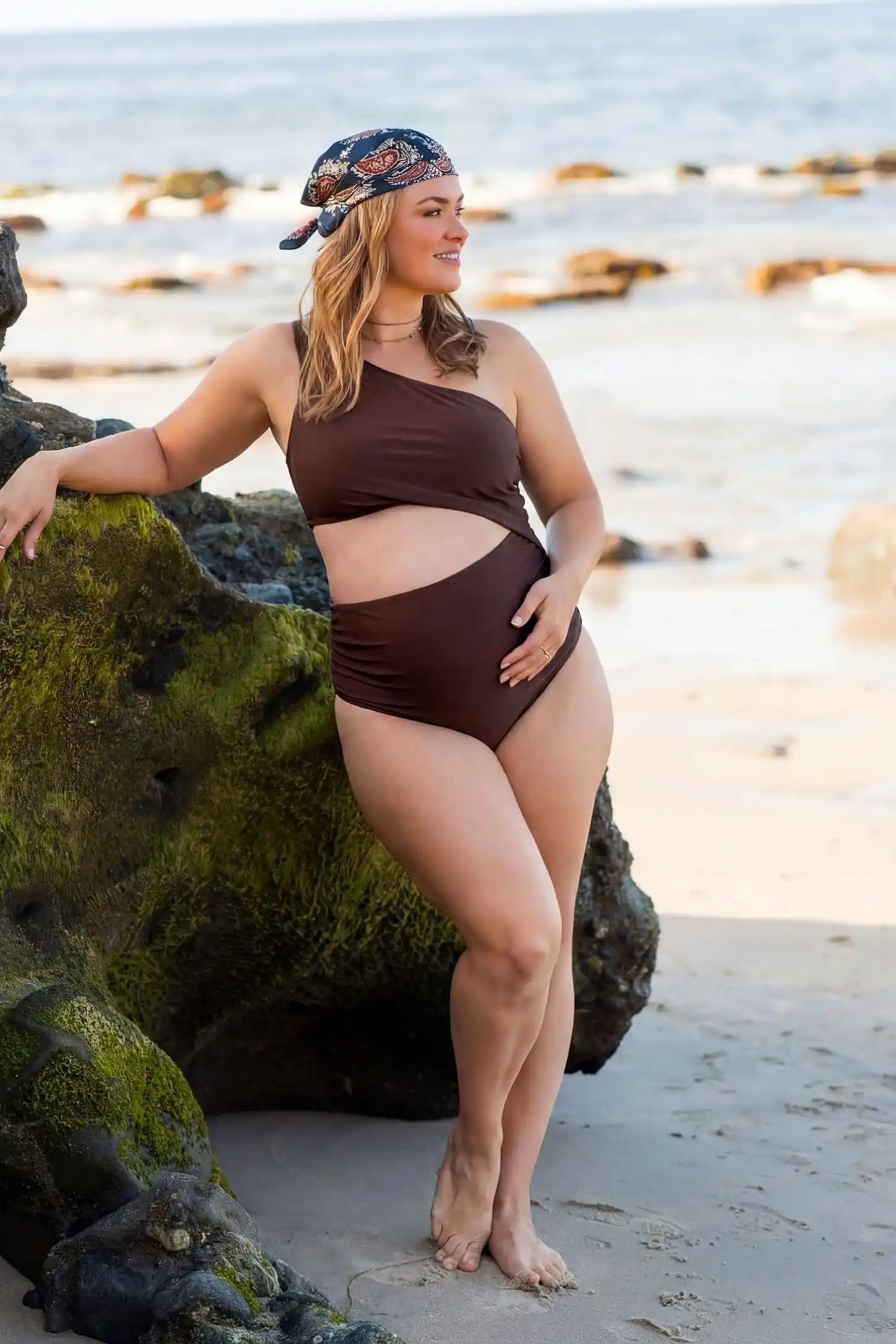 One-Shoulder Cutout Maternity Monokini One-Shoulder Cutout Maternity Monokini in Brown featuring premium swim fabric on a pregnant model, outdoor lifestyle view.