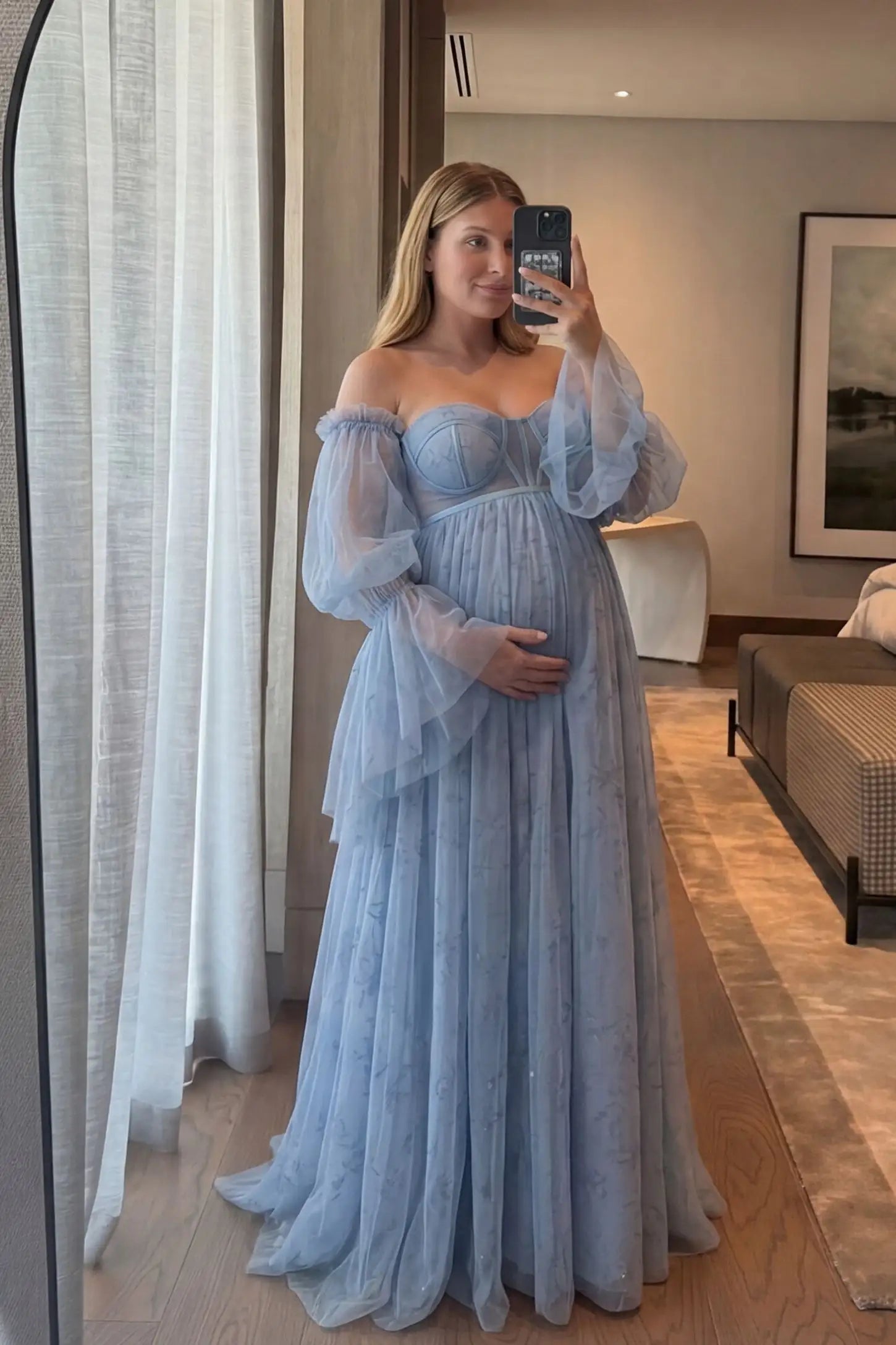 Organza Tie-Back Off-Shoulder Long Sleeve Maternity Gown Organza Tie-Back Off-Shoulder Maternity Gown in Blue featuring an A-line tulle skirt on a pregnant model in a mirror selfie.