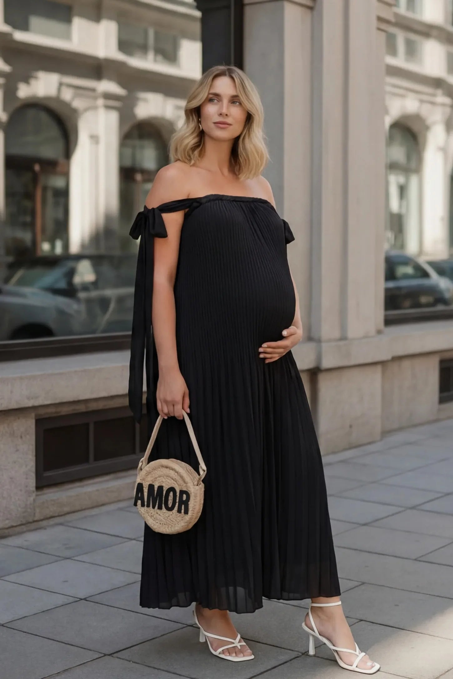 Pleated Braided Cold-Shoulder Maxi Maternity Gown Pleated Braided Cold-Shoulder Maxi Maternity Gown in Black featuring soft pleated fabric on a pregnant model in an editorial lifestyle setting.