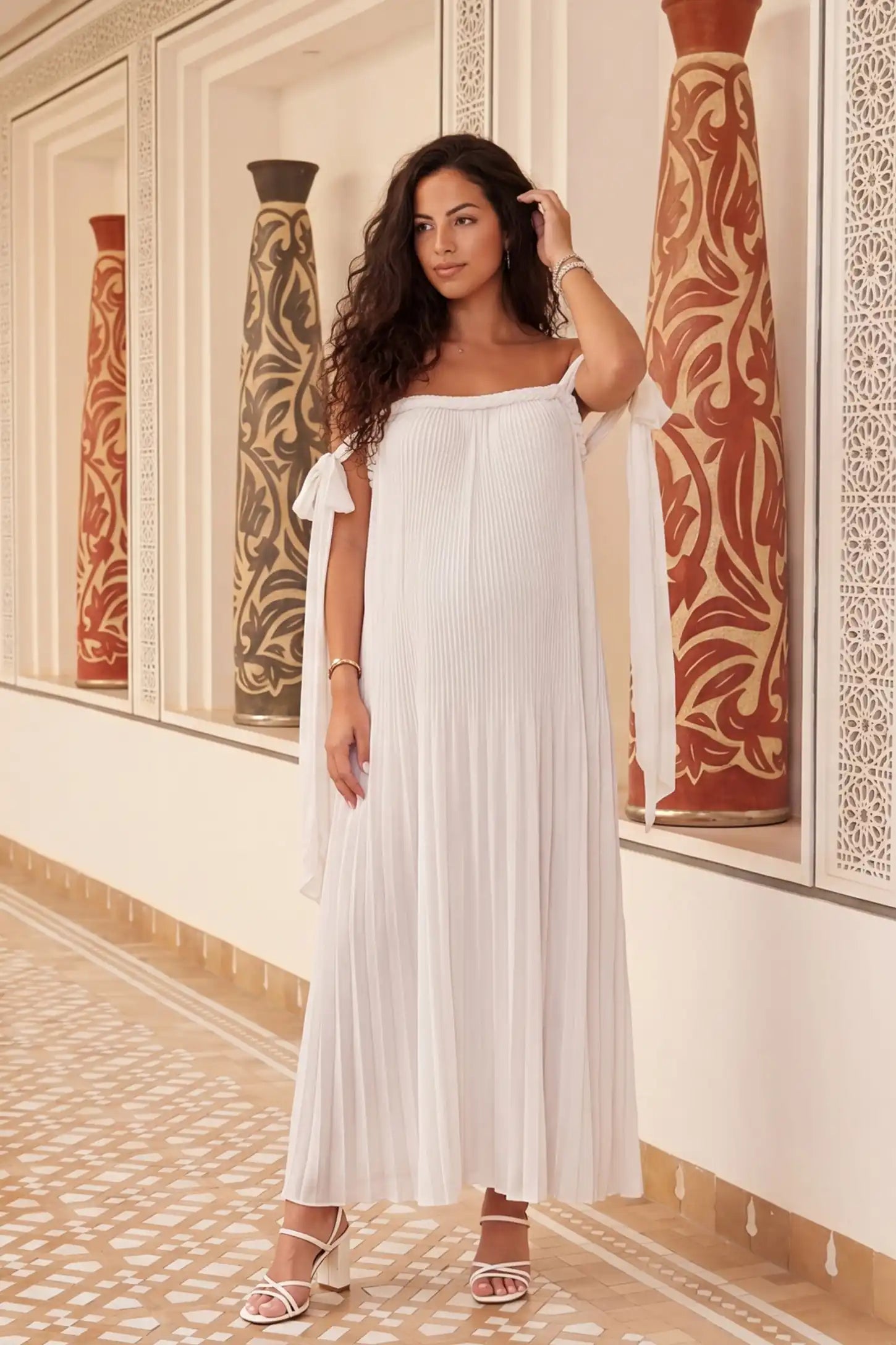 Pleated Braided Cold-Shoulder Maxi Maternity Gown Pleated Braided Cold-Shoulder Maxi Maternity Gown in White featuring soft pleated fabric on a pregnant model in an editorial lifestyle setting.